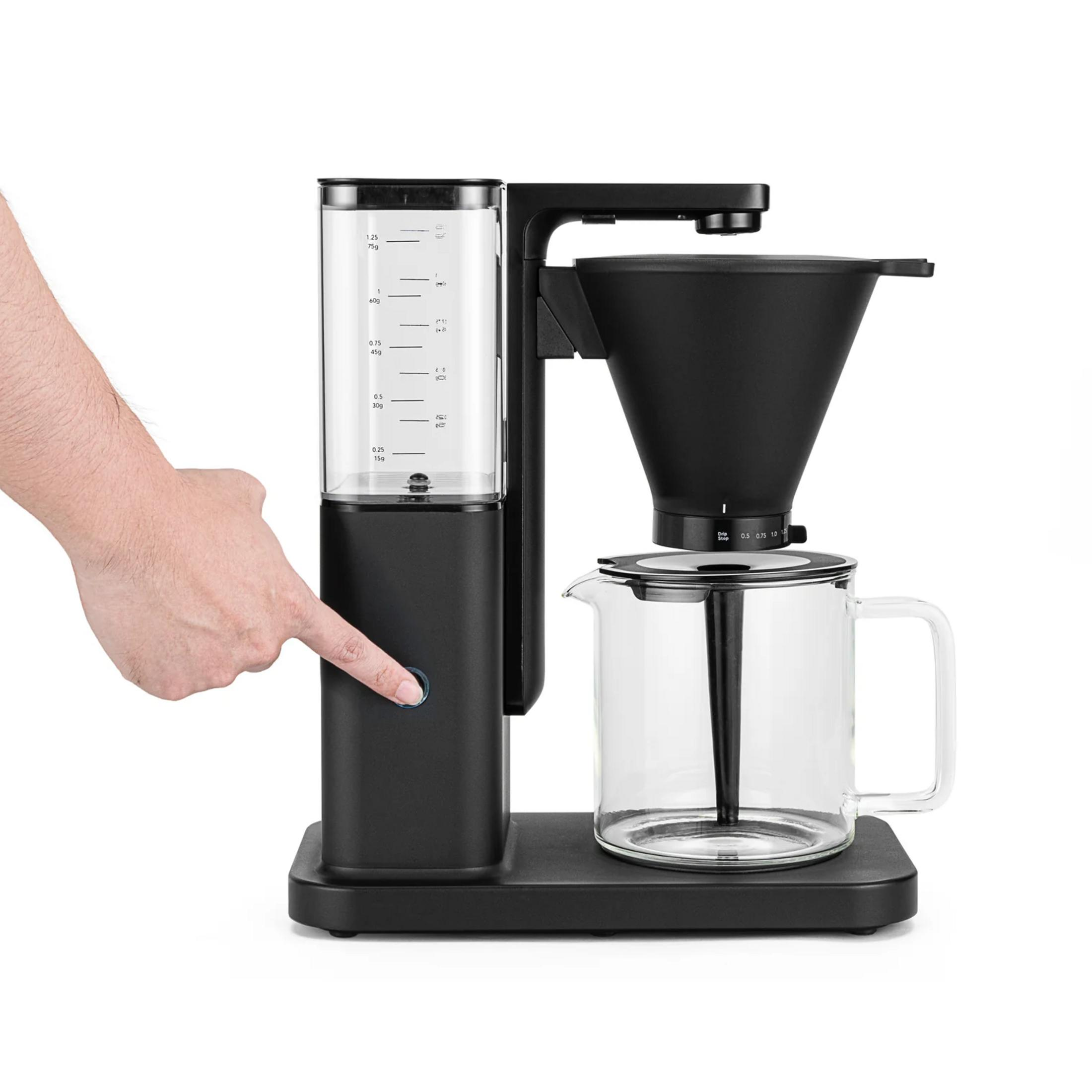 Eine Hand drückt einen Knopf an einer schwarzen Kaffeemaschine mit Glaskanne.