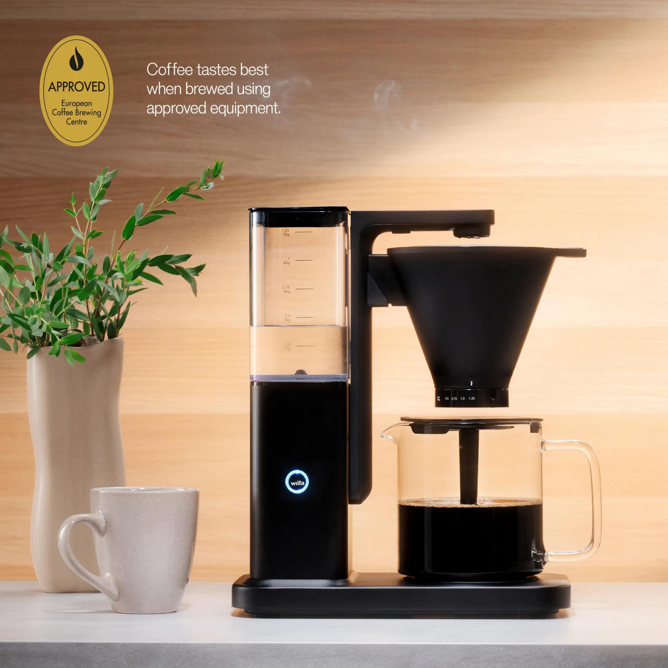 Schwarze Kaffeemaschine mit Glaskaraffe, gefüllt mit Kaffee, und einer grauen Tasse.