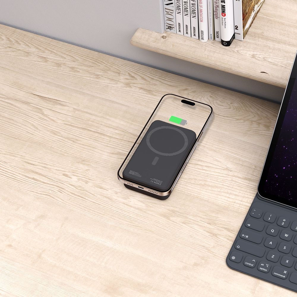 Ein schwarzes Handy mit einer Powerbank liegt auf einem Holztisch.