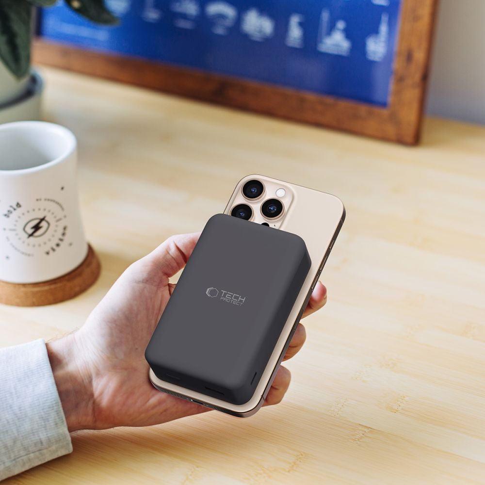 Eine Hand hält ein Smartphone mit einer dunklen Powerbank auf der Rückseite.