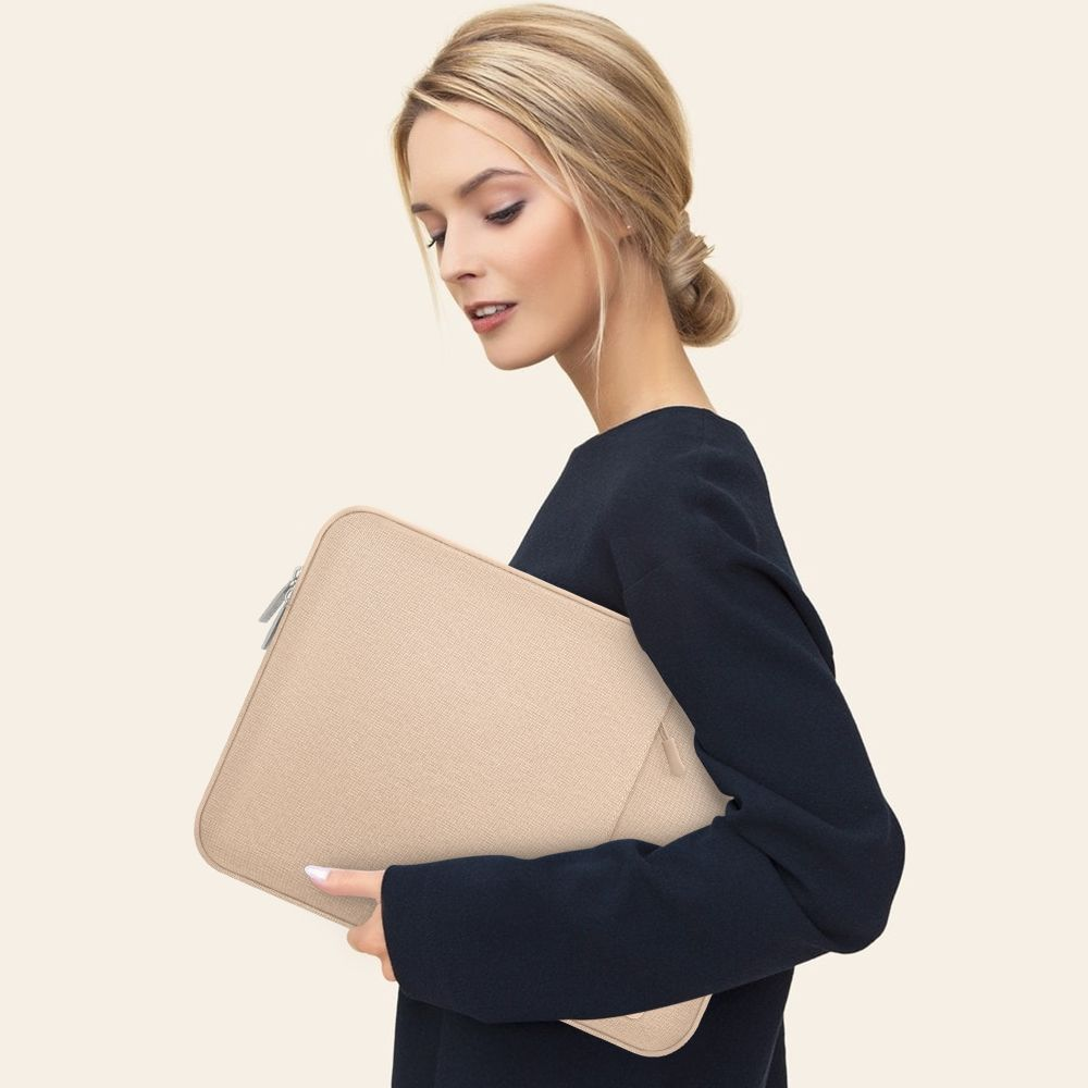 Eine Frau in einem dunkelblauen Kleid hält eine beige Laptoptasche.