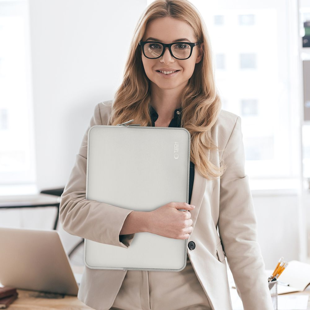 Eine Frau in einem beigen Anzug hält eine weiße Laptoptasche vor sich.