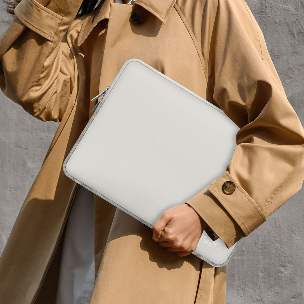 Eine Person in einem beigen Trenchcoat hält eine hellgraue Laptoptasche. Die Tasche hat einen Reißverschluss.