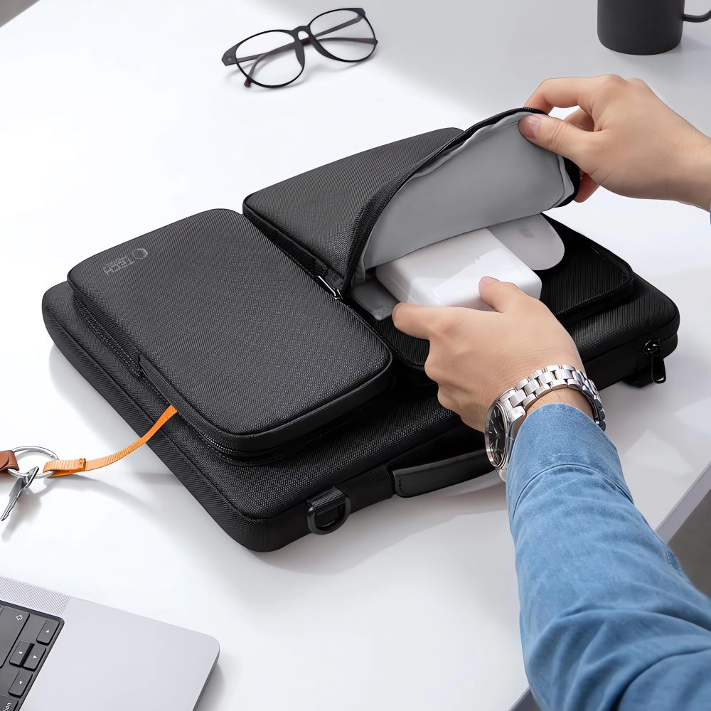 Person packt weiße Ladegeräte in schwarze Tasche neben Laptop und Brille.
