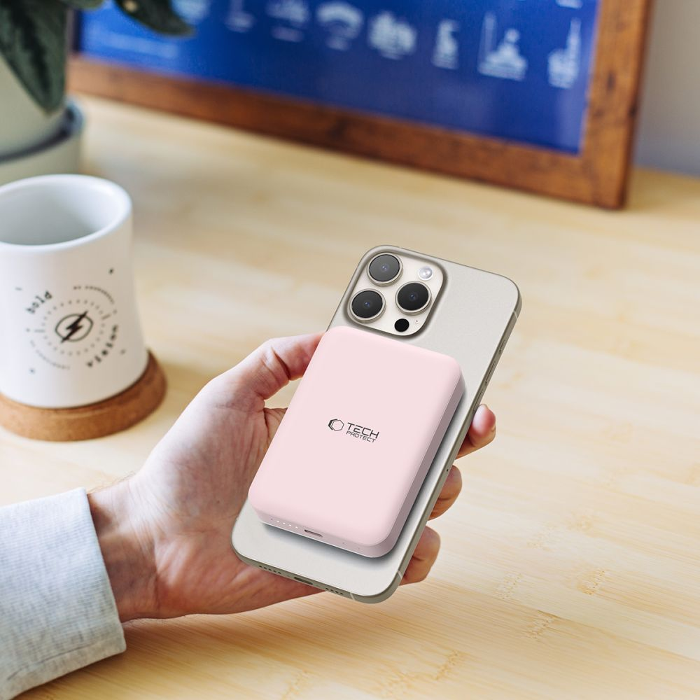 Eine Hand hält ein hellgraues Smartphone mit einer rosa Powerbank darauf.