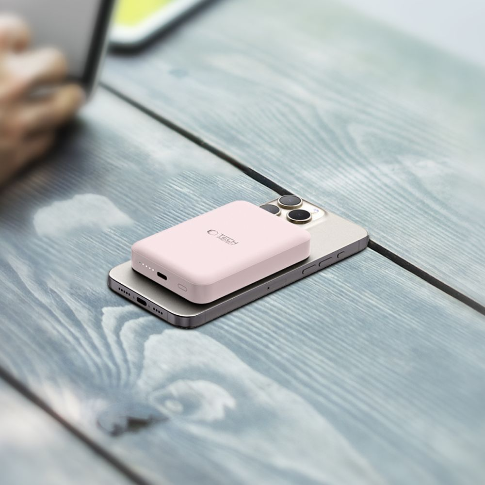 Ein rosafarbener Akku liegt auf einem Smartphone auf einem Holztisch.
