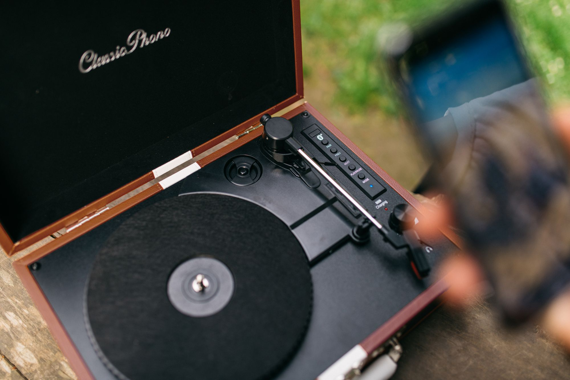 Gramofon z otwartą pokrywą stoi na drewnie. Telefon na pierwszym planie.