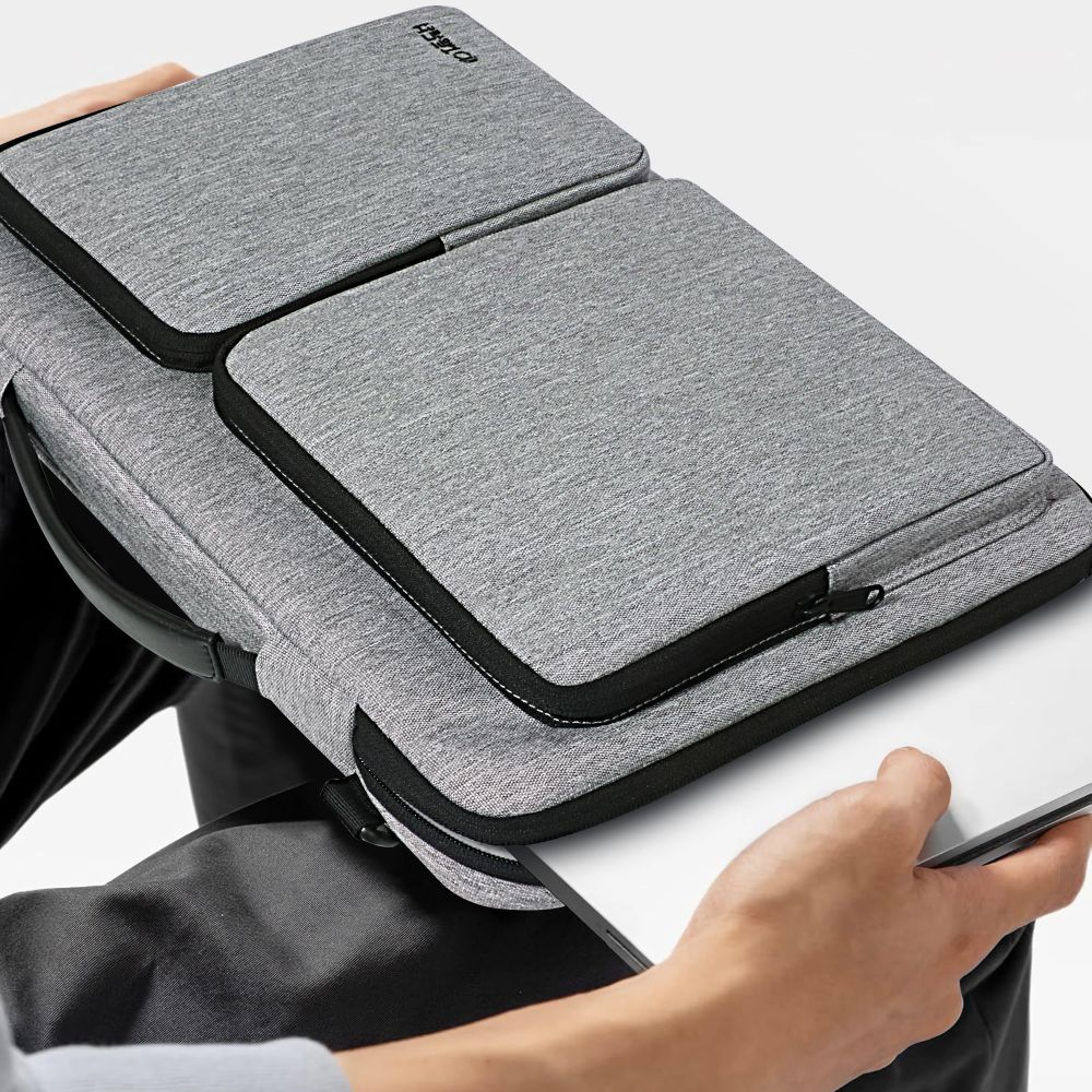 Graue Laptoptasche mit schwarzem Reißverschluss, gehalten von Person.