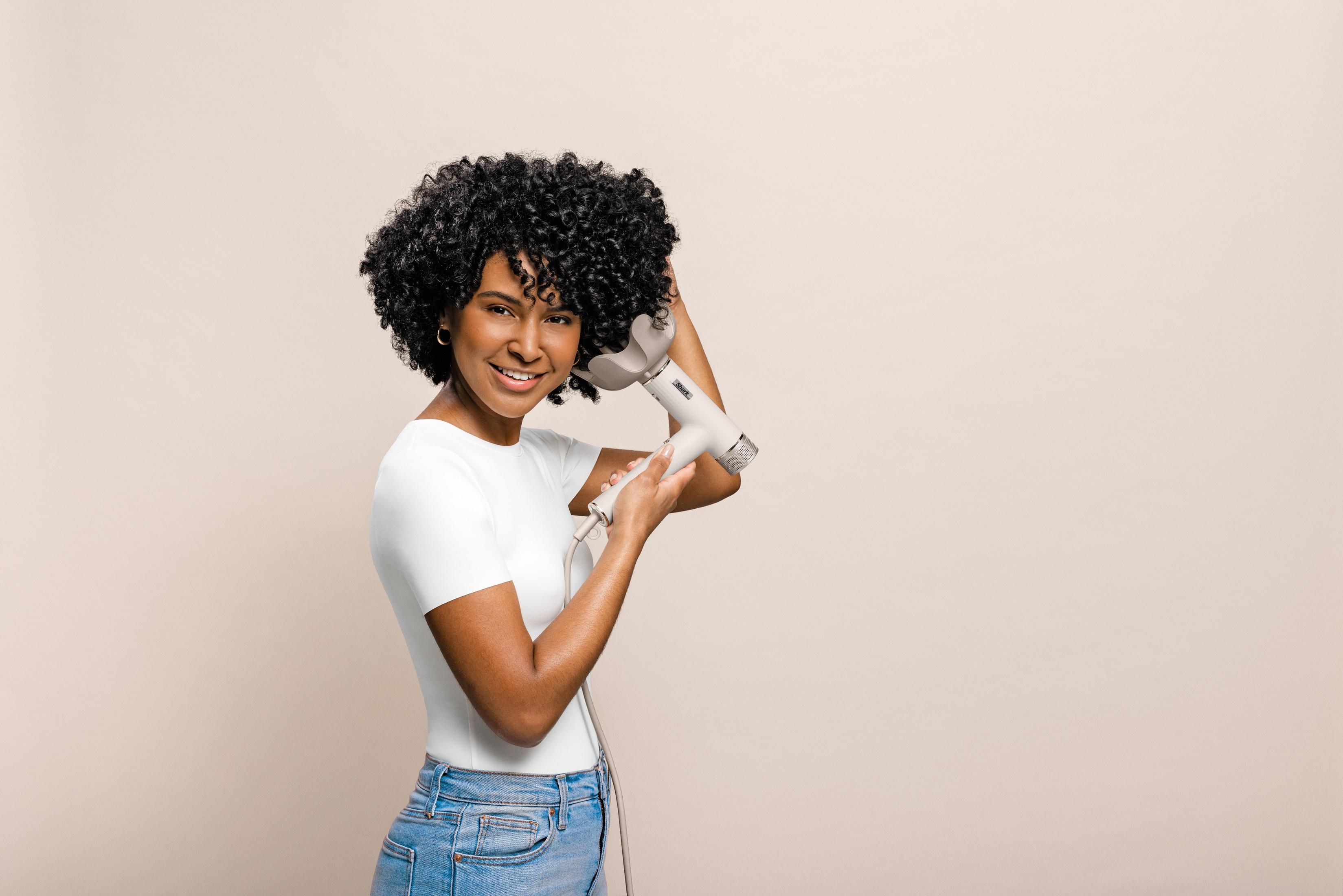 Kobieta z kręconymi włosami suszy włosy białym suszarką.