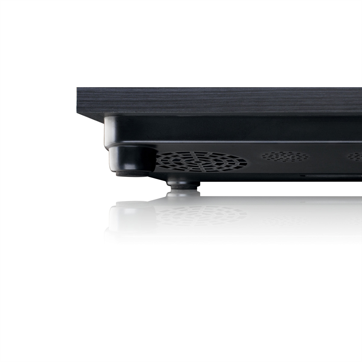 Czarne urządzenie z otworami wentylacyjnymi i gumowymi nóżkami, odbija się na białej powierzchni.