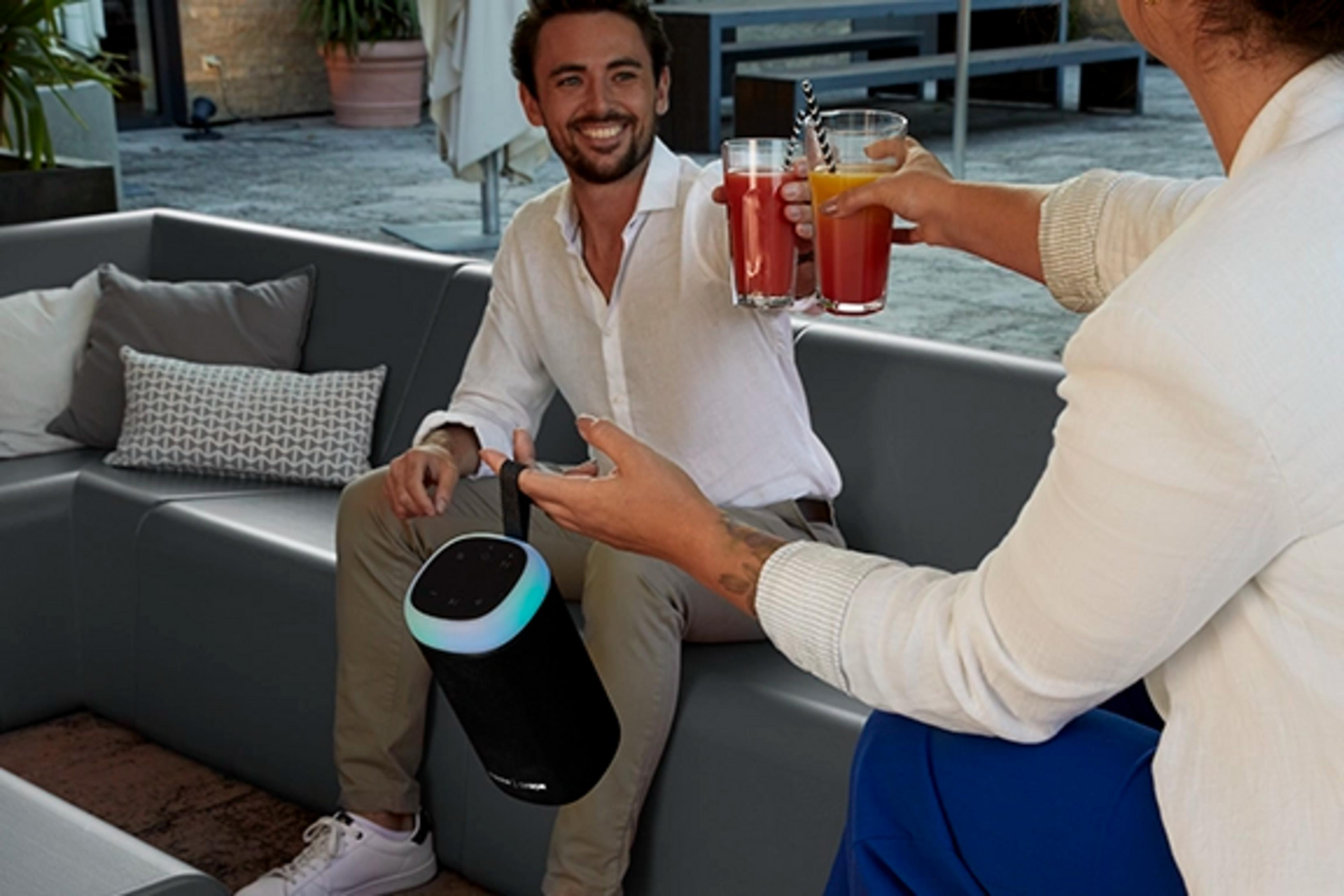 Mężczyzna i kobieta wznoszą toast napojami, czarny głośnik ze światłem.