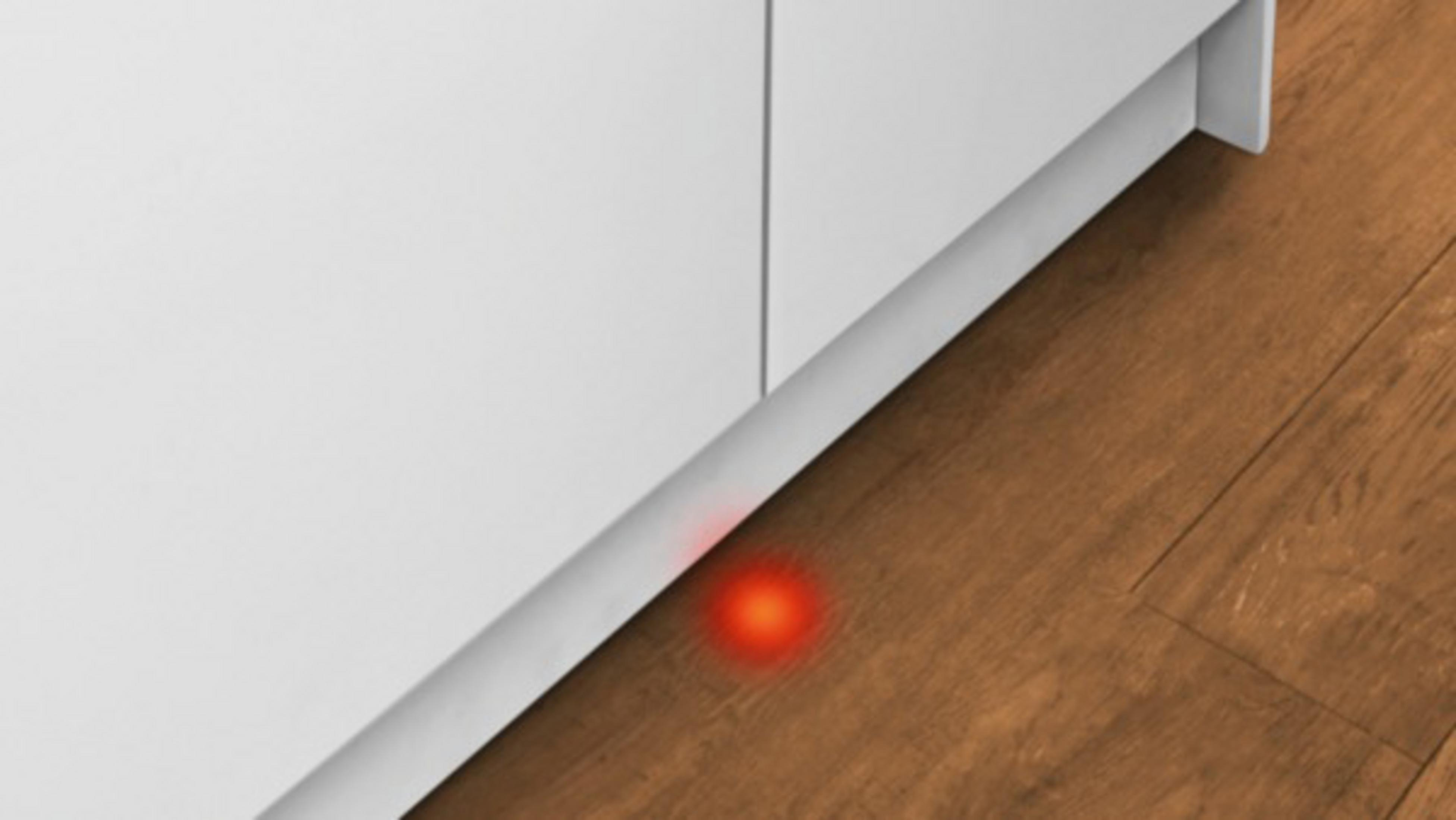 Un punto di luce rosso brilla su un pavimento in legno accanto a un mobile bianco.