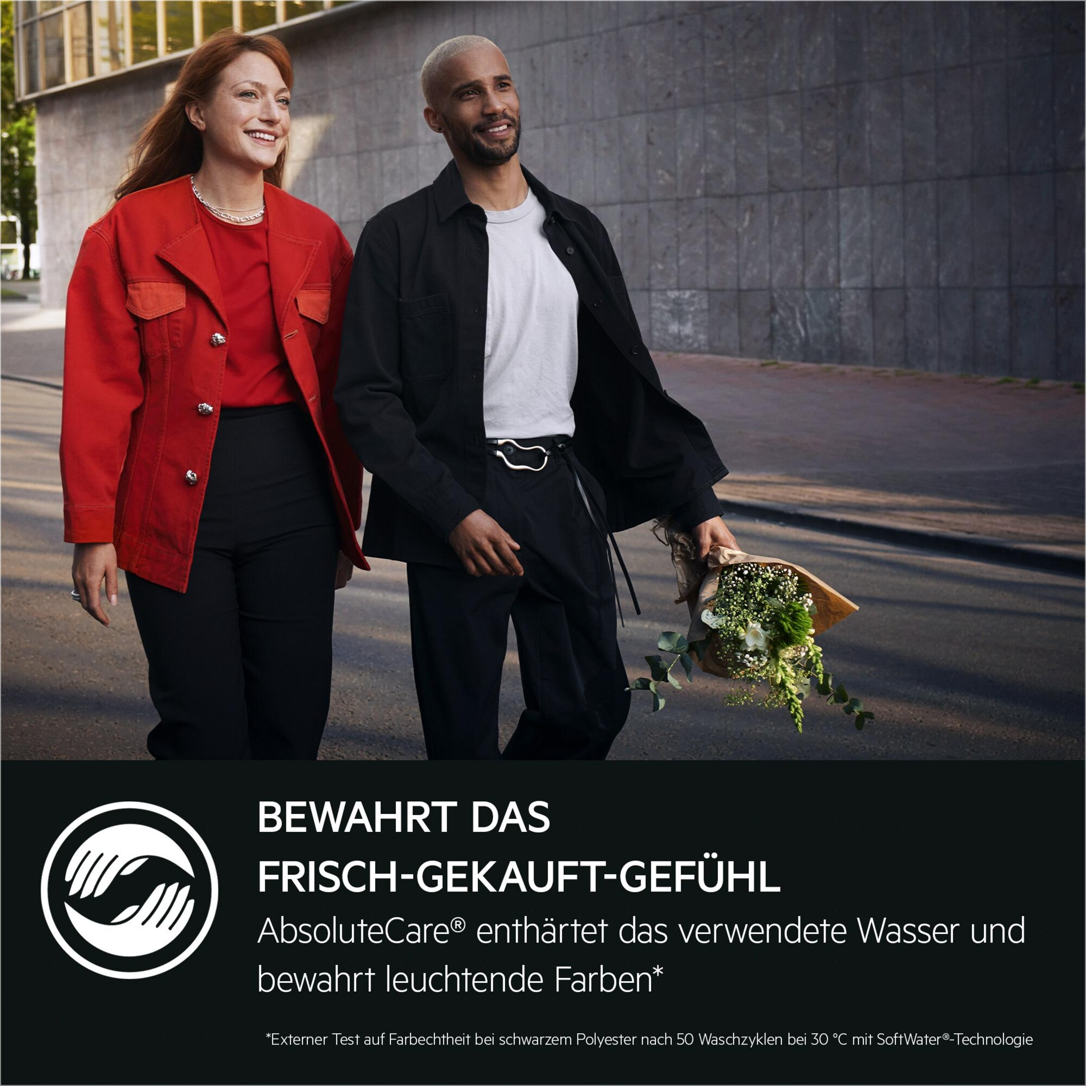 Ein Mann und eine Frau gehen in der Stadt spazieren, er trägt Blumen. Die Kleidung ist modern.
