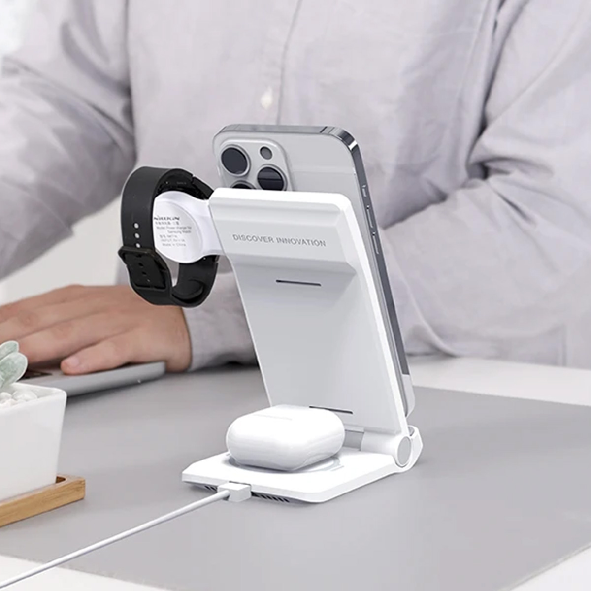 Ein Mann lädt ein Smartphone, eine Smartwatch und Ohrhörer auf einem weißen Ladegerät auf.