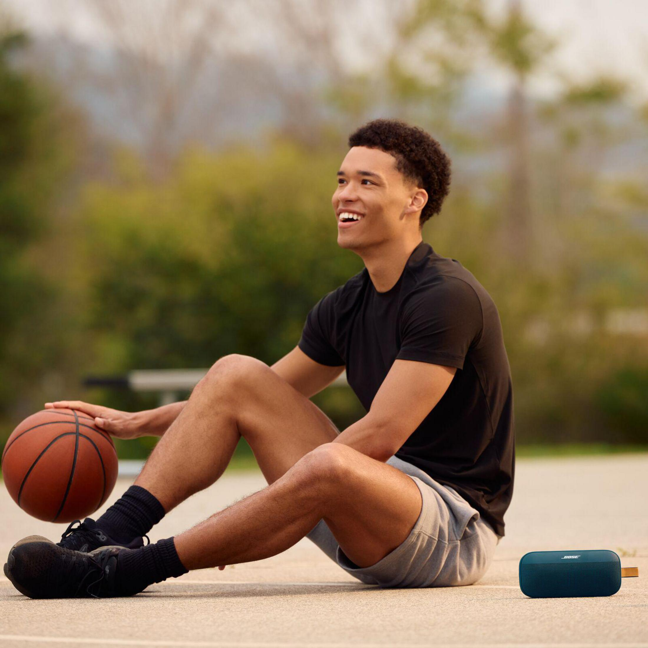 Ein Mann sitzt auf einem Basketballplatz mit einem Ball und einem Lautsprecher.