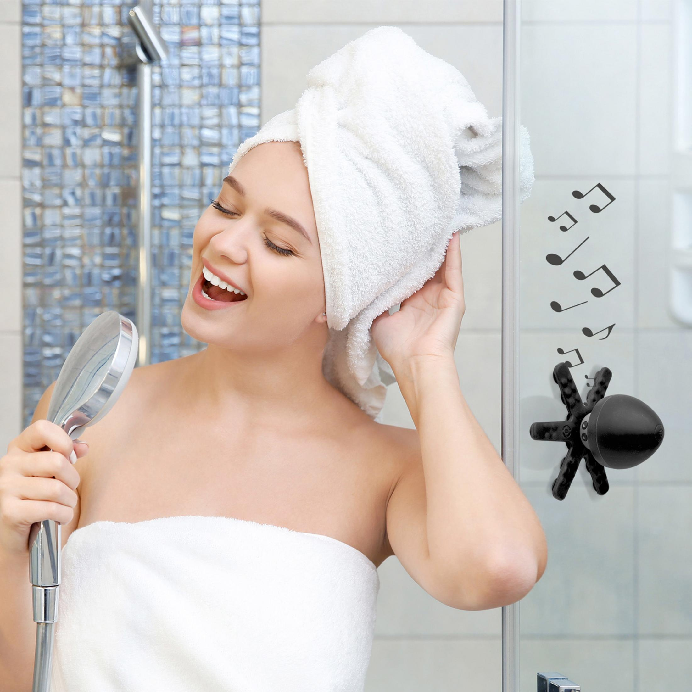 Kobieta śpiewa z słuchawką prysznicową, ręcznik na głowie.