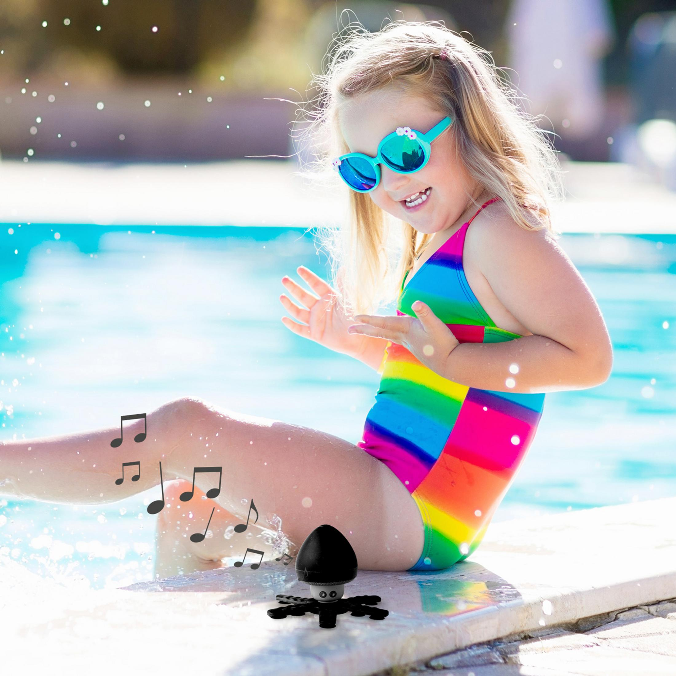Dziewczynka w kolorowym stroju kąpielowym i okularach przeciwsłonecznych siedzi przy basenie.