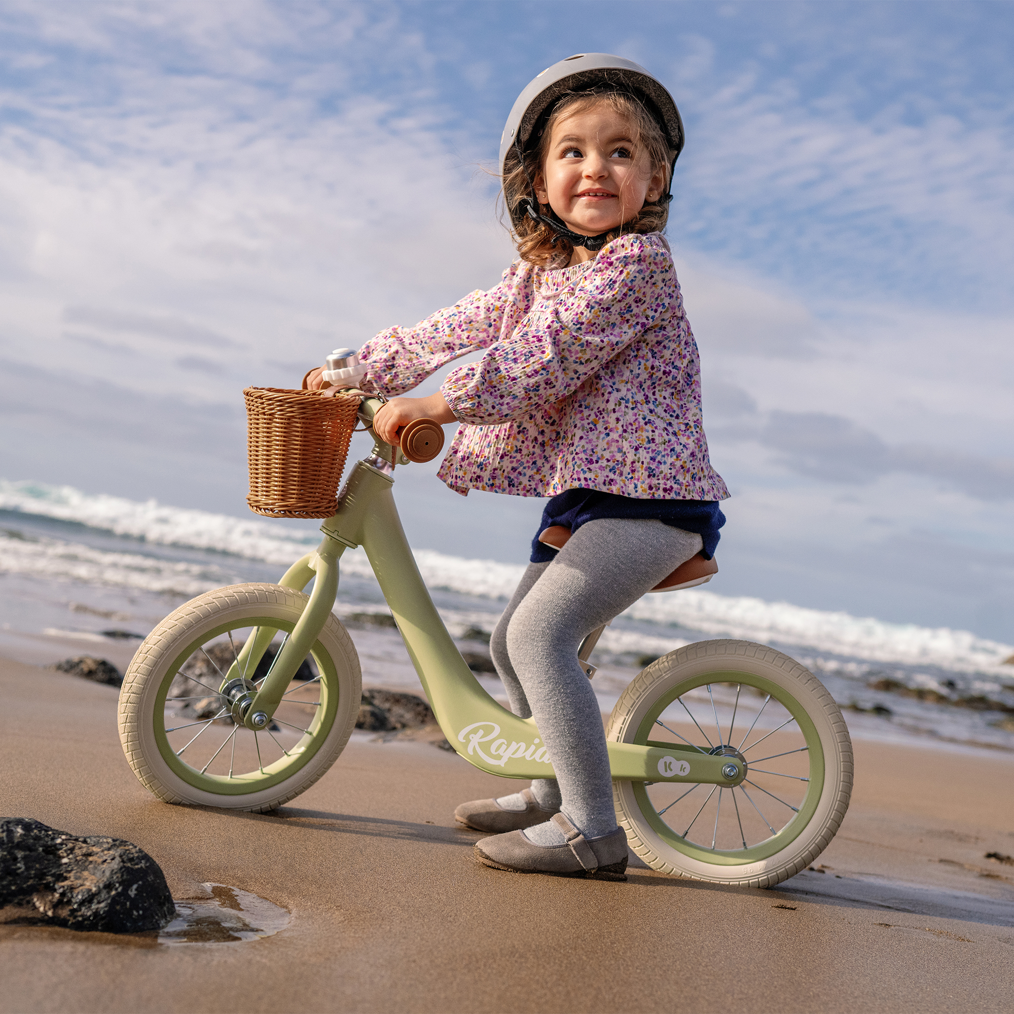 Ein Mädchen mit Helm fährt ein Laufrad am Strand.