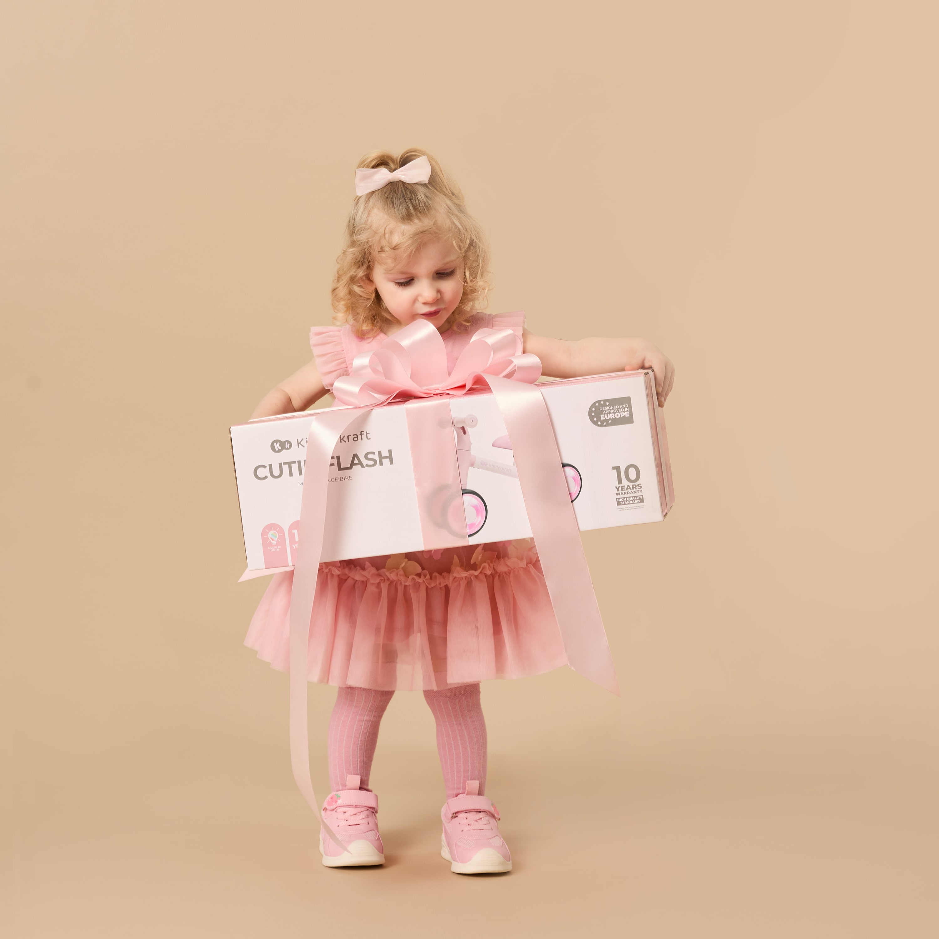 Ein kleines Mädchen im rosa Kleid hält eine Geschenkbox mit Schleife.