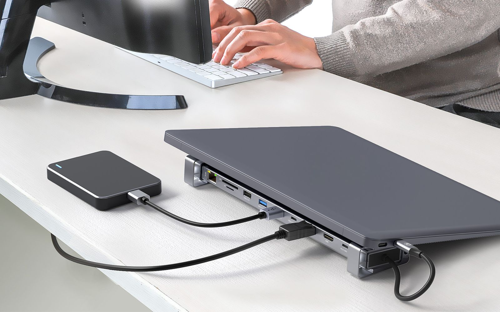 Eine Laptop-Dockingstation verbindet sich mit einem Laptop und einer externen Festplatte auf einem Schreibtisch.