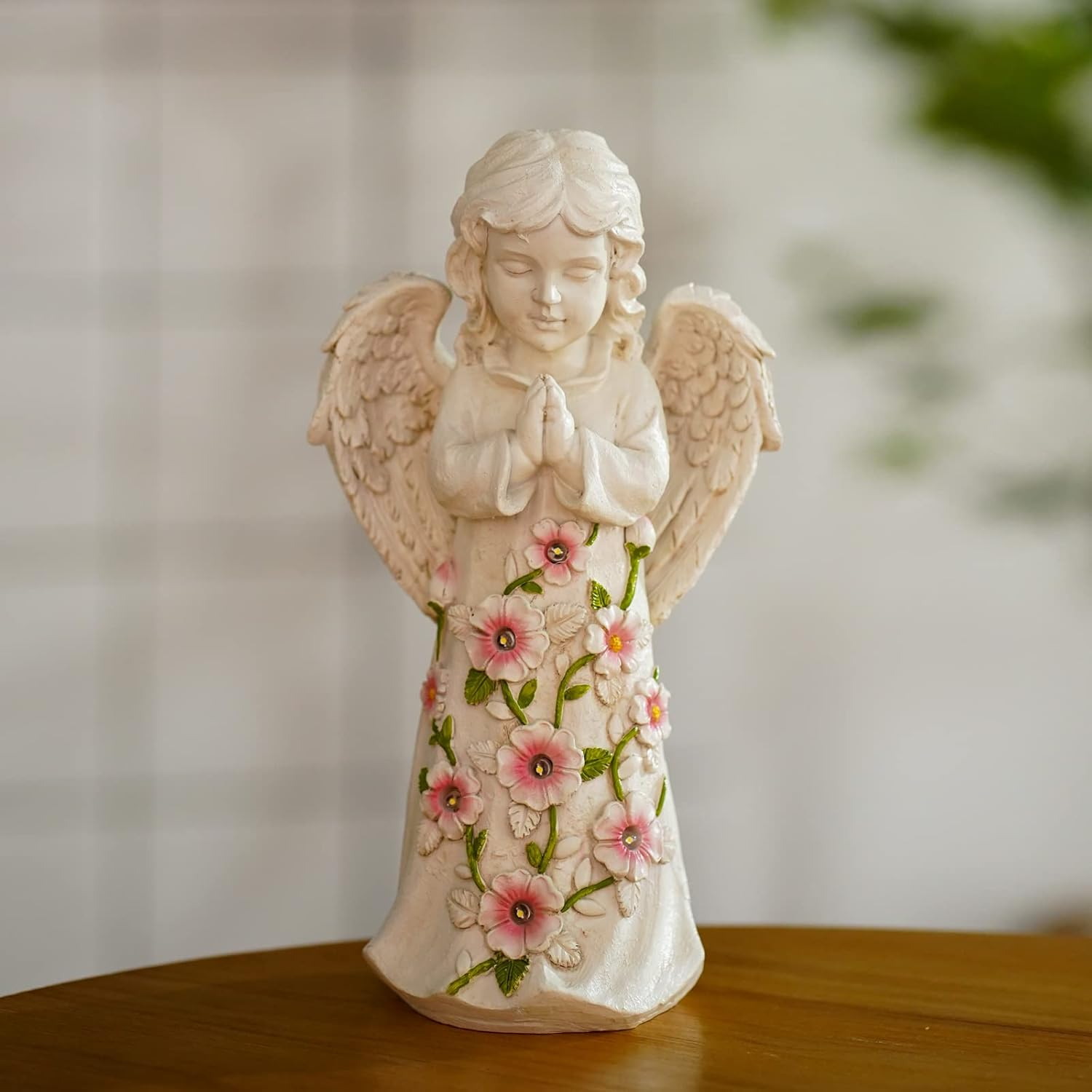 Eine weiße Engelsstatue mit rosa Blumen und grünen Blättern auf dem Kleid.