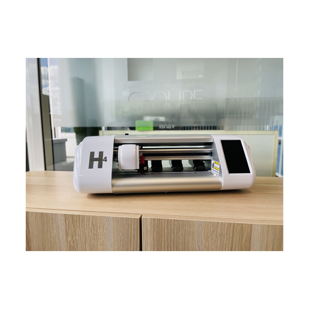 Ein weißer H4-Schneideplotter mit Metallgehäuse auf einem Holzschrank.
