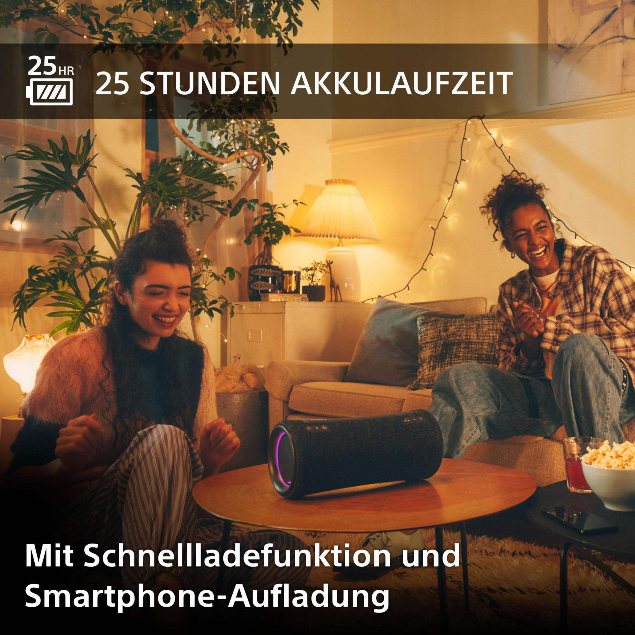 Zwei Frauen lachen auf einem Sofa, ein Lautsprecher steht auf dem Tisch.