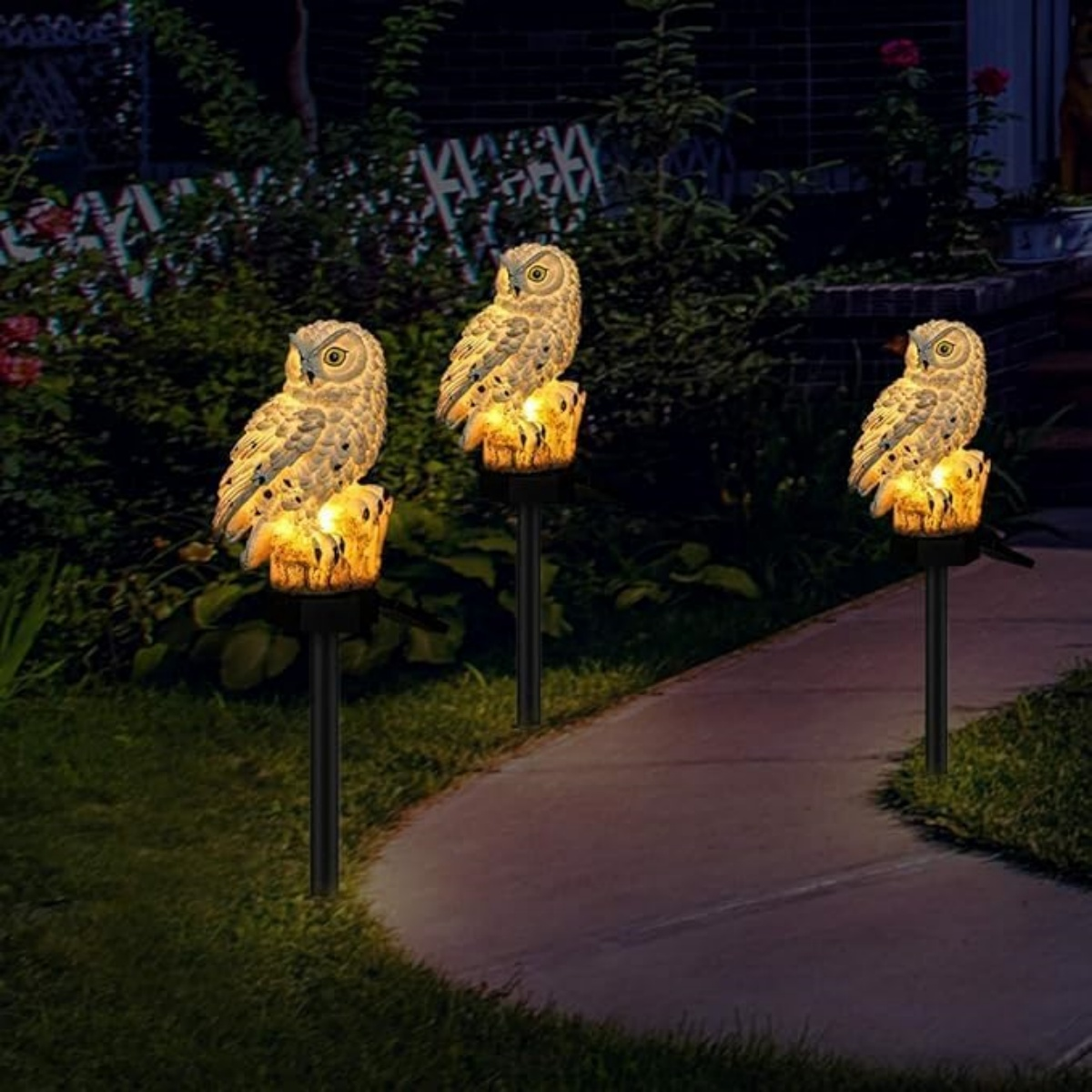 Drei Eulen-Solarleuchten beleuchten einen Weg im Garten bei Nacht.