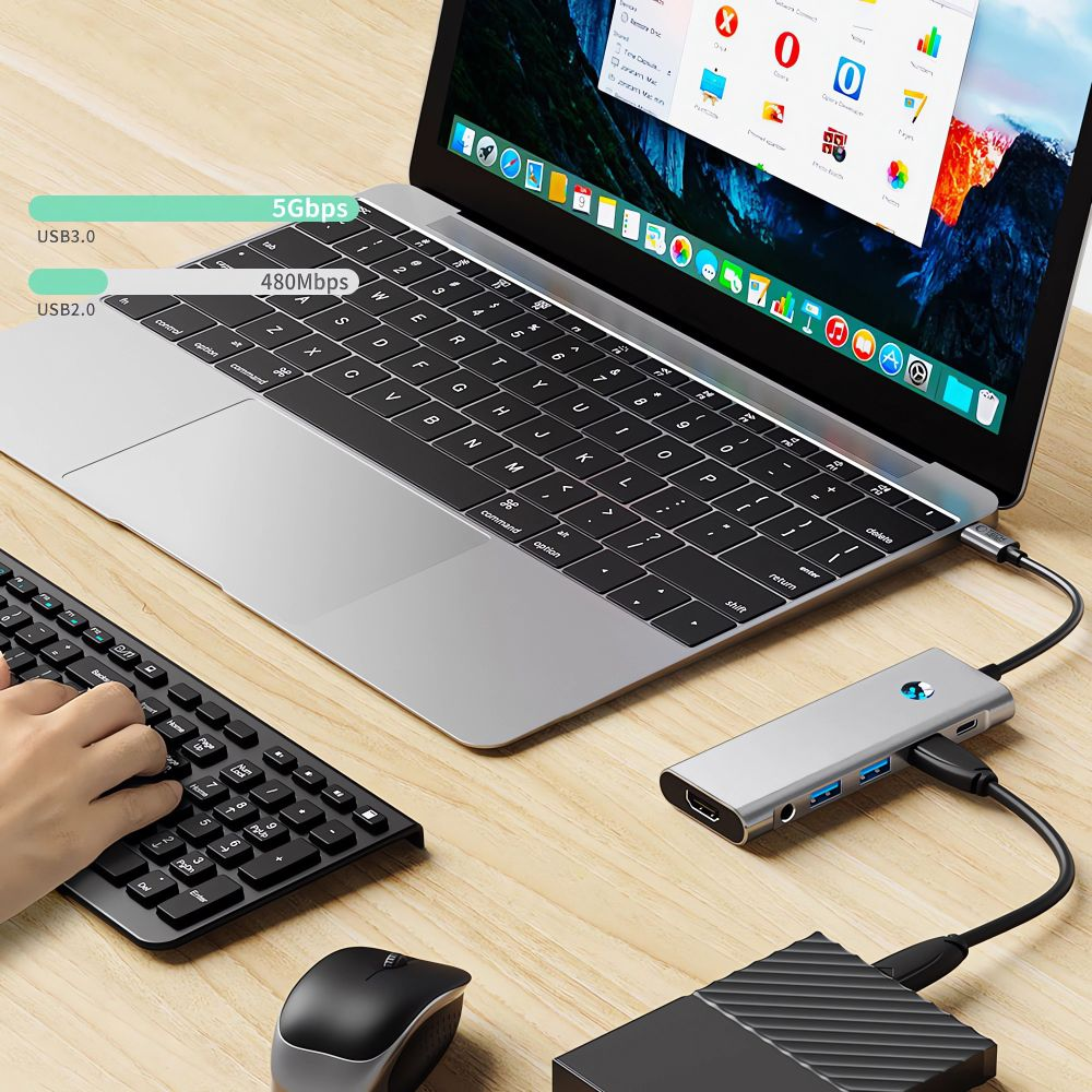 Laptop con hub USB, tastiera, mouse e disco esterno su una scrivania di legno.