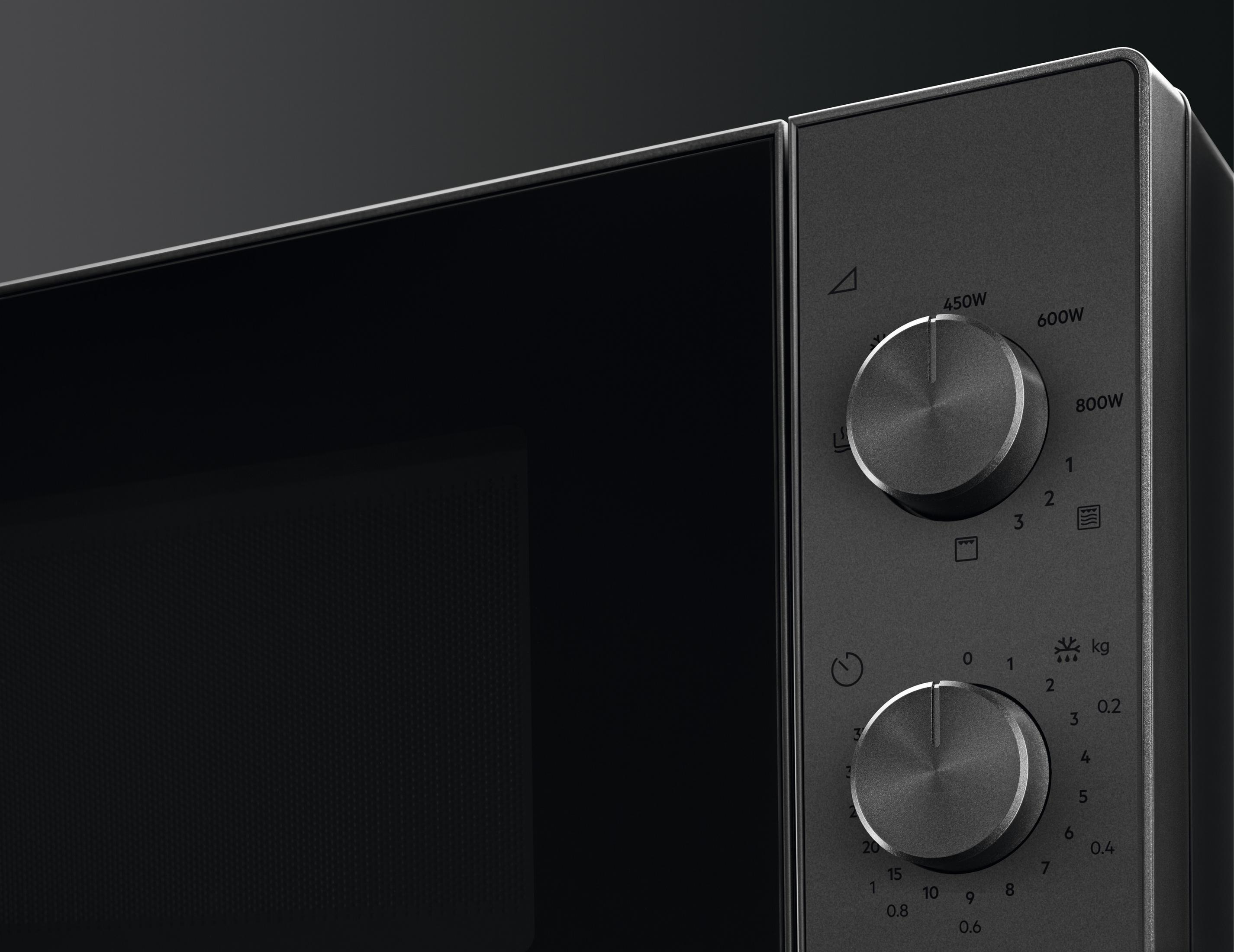 Zbliżenie czarnej kuchenki mikrofalowej z dwoma pokrętłami do ustawień mocy i czasu.