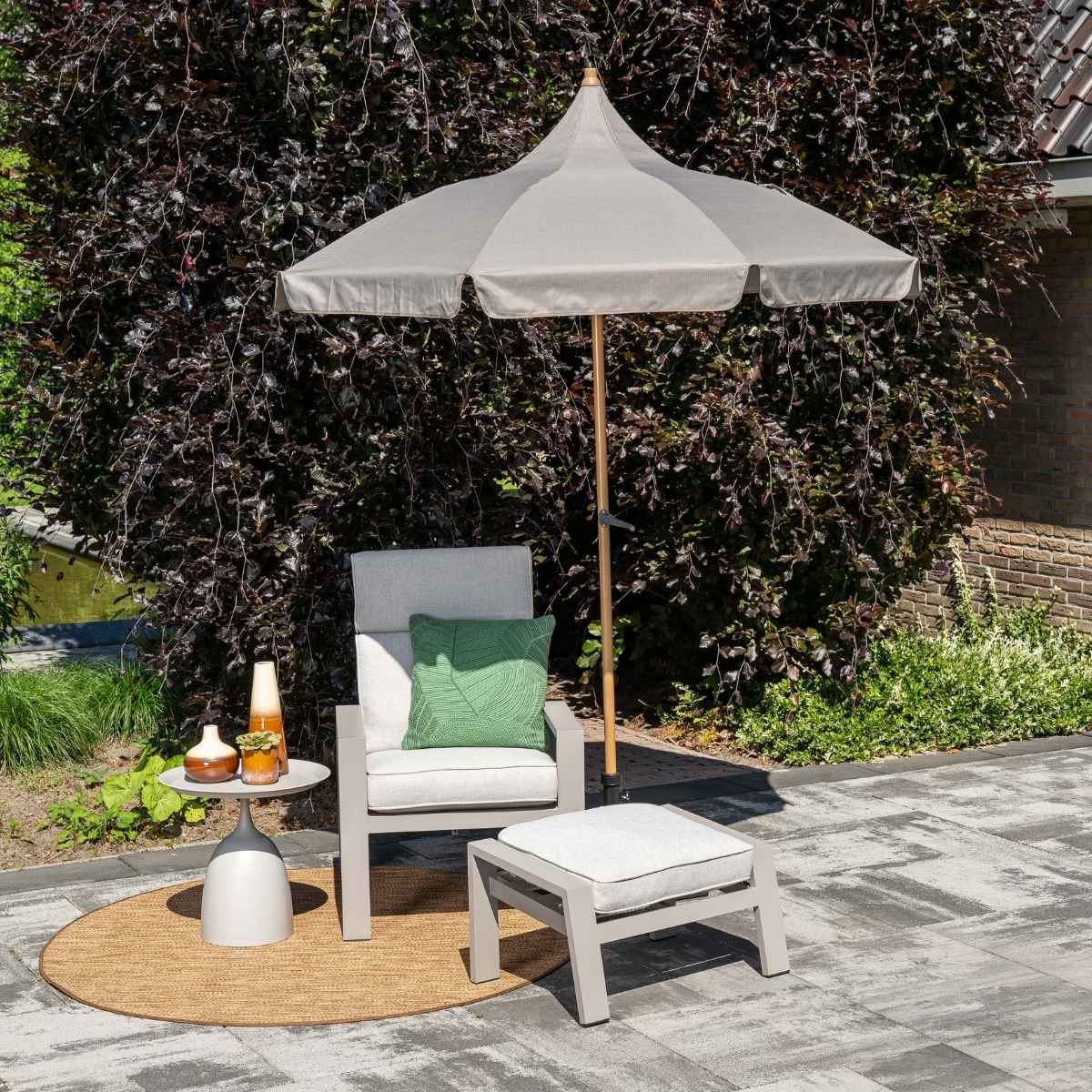 Een grijze fauteuil met kussen en hocker onder een parasol.