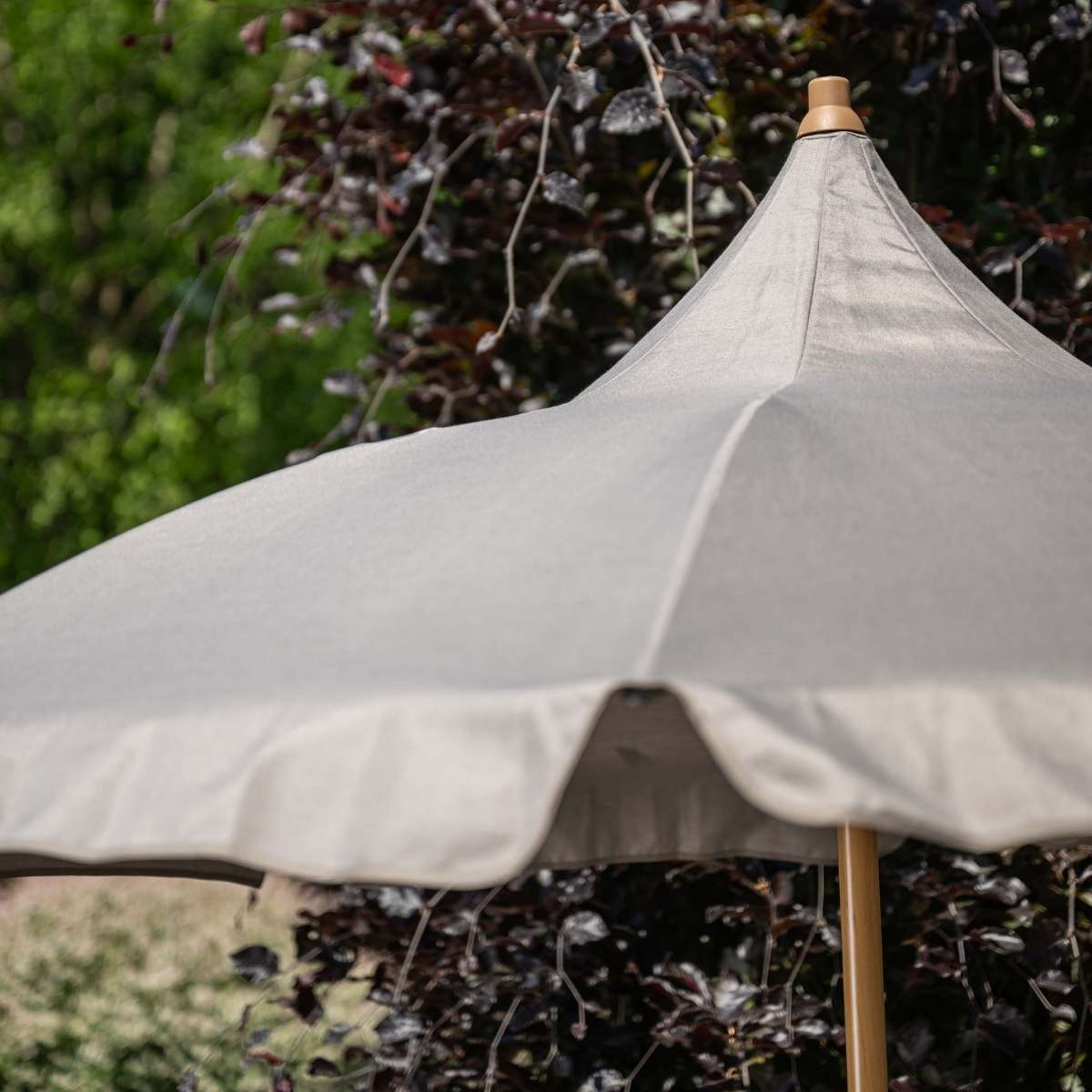 Een grijze parasol met houten paal staat buiten in het groen.