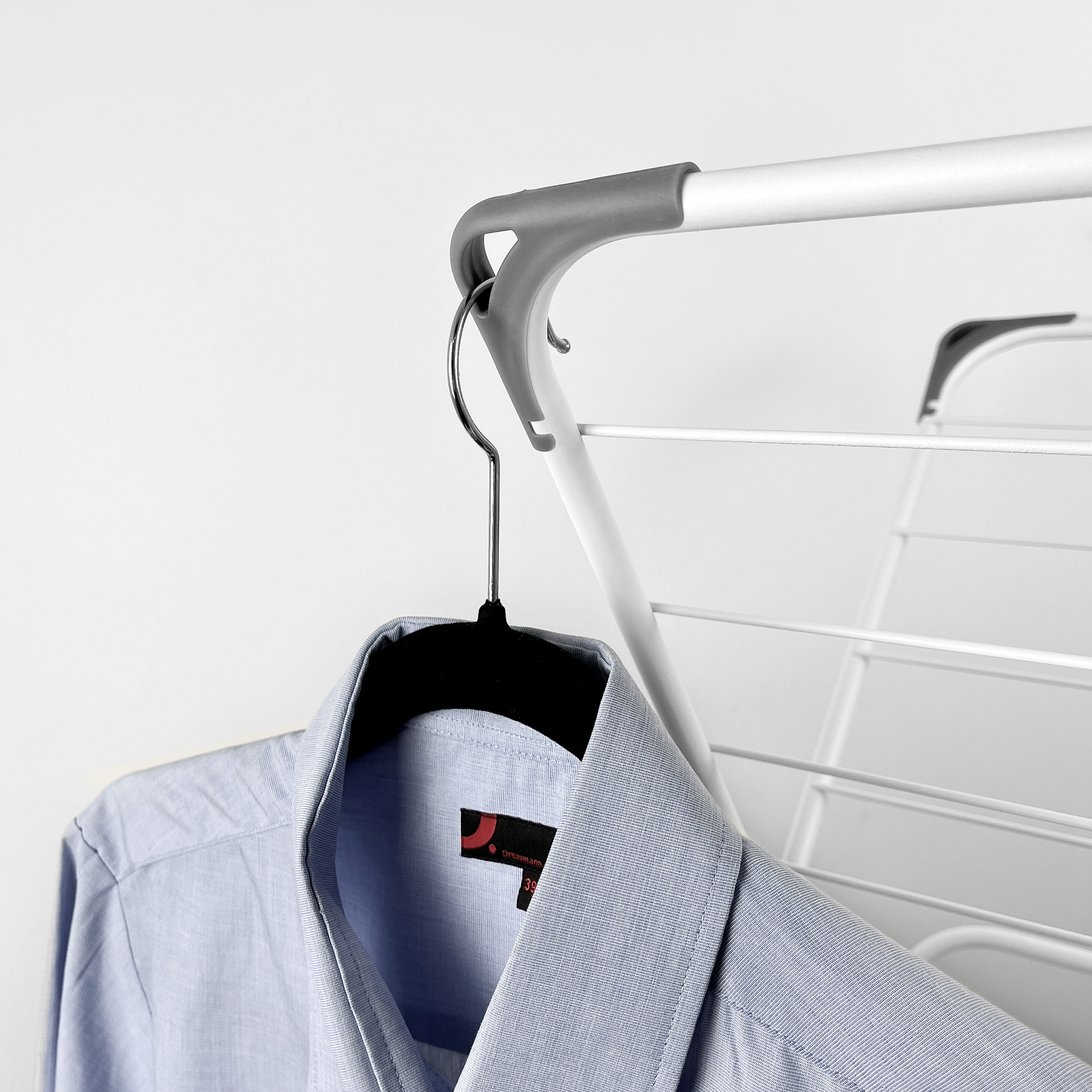 A light blue shirt hangs on a black hanger on a drying rack.