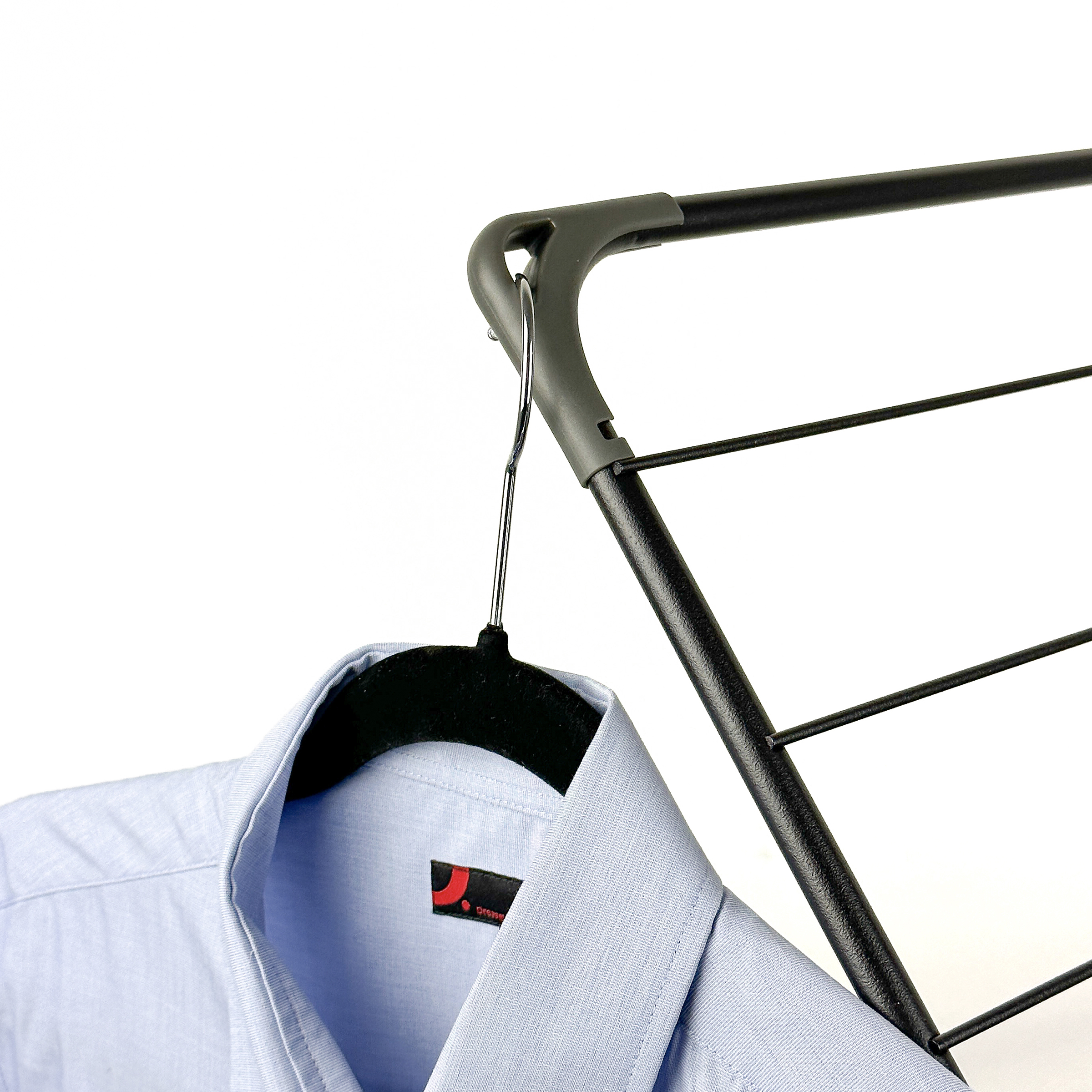 A light blue shirt hangs on a black hanger on a drying rack.