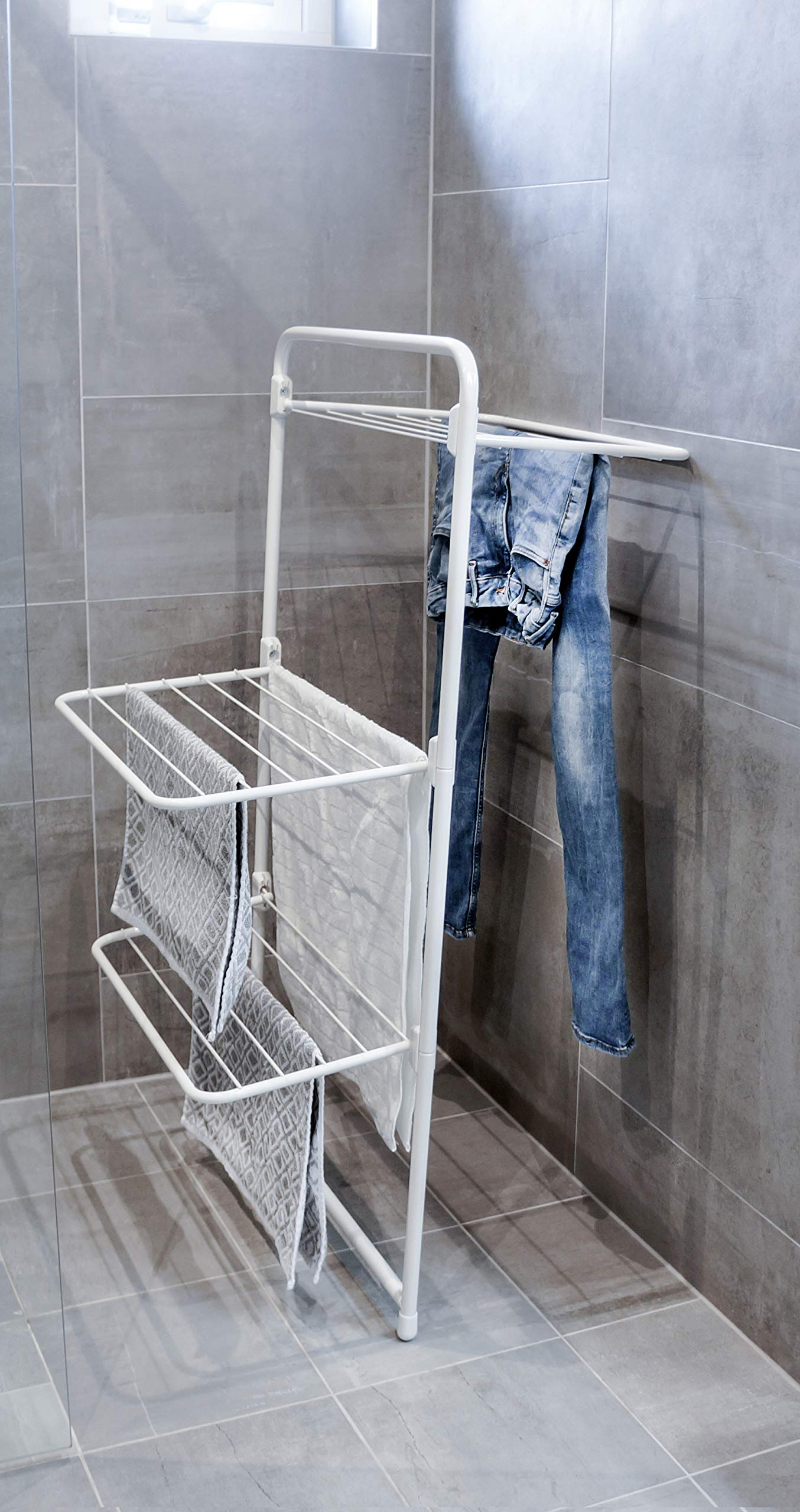 Un étendoir blanc avec un jean et des serviettes dans une salle de bain.
