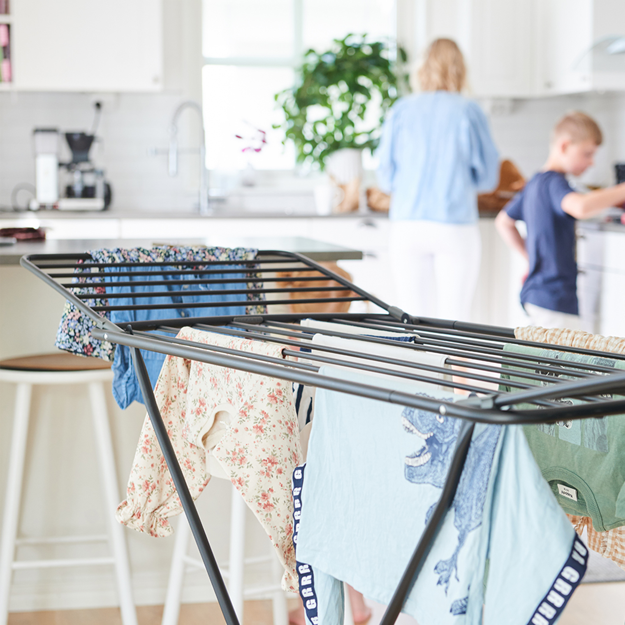 Étendoir à linge avec vêtements. Personnes et cuisine à l'arrière-plan.