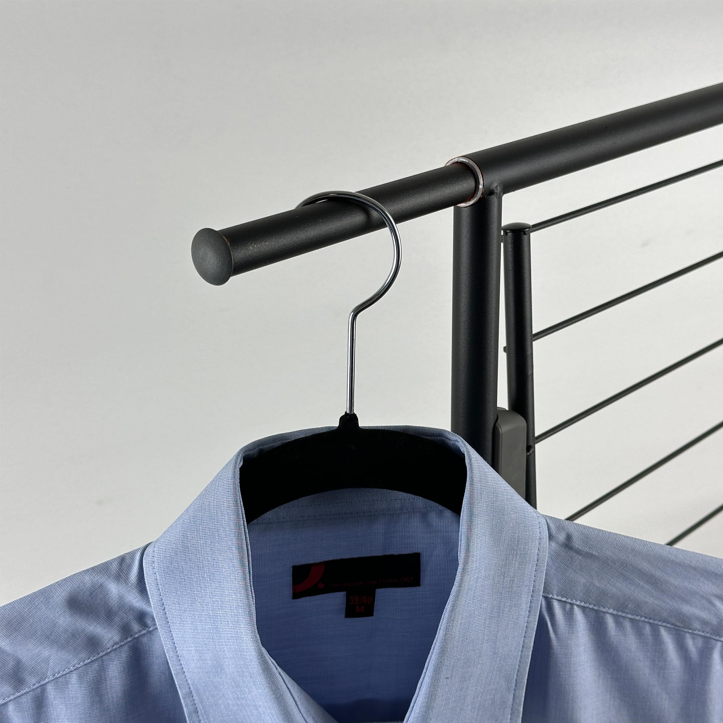 Une chemise habillée bleu clair est suspendue à un cintre noir sur un portant.