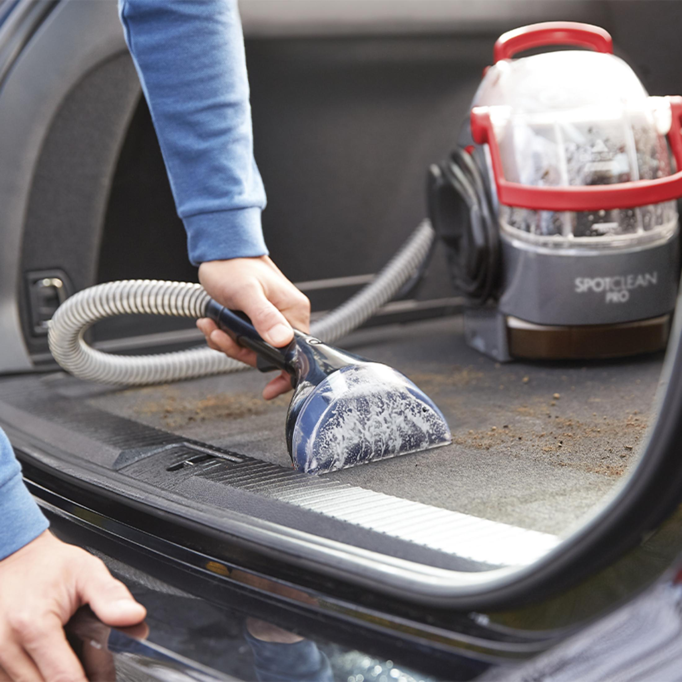 Osoba czyści dywanik bagażnika samochodu urządzeniem.