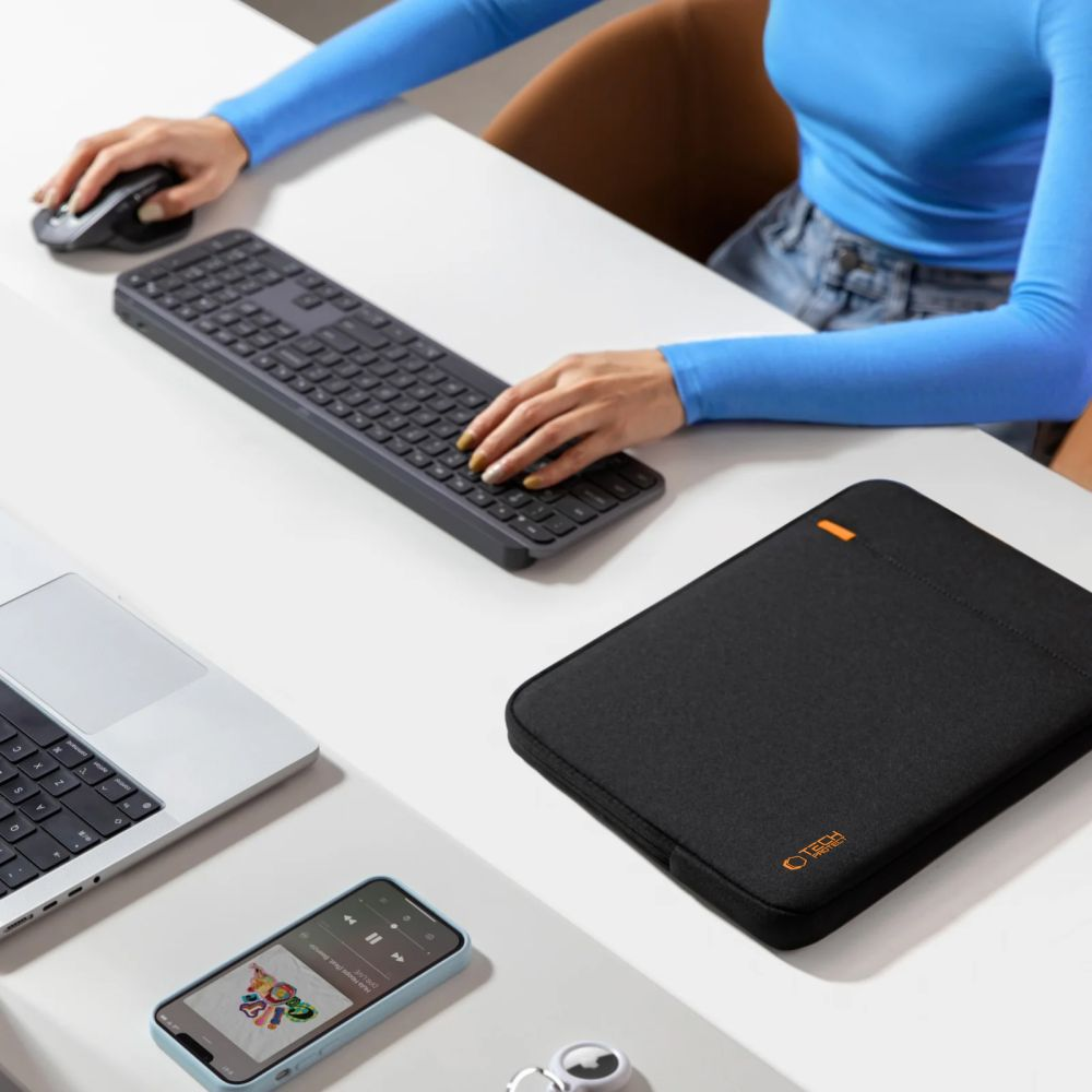 Eine Person tippt auf einer Tastatur, daneben Laptop, Handy, Maus und eine Hülle.