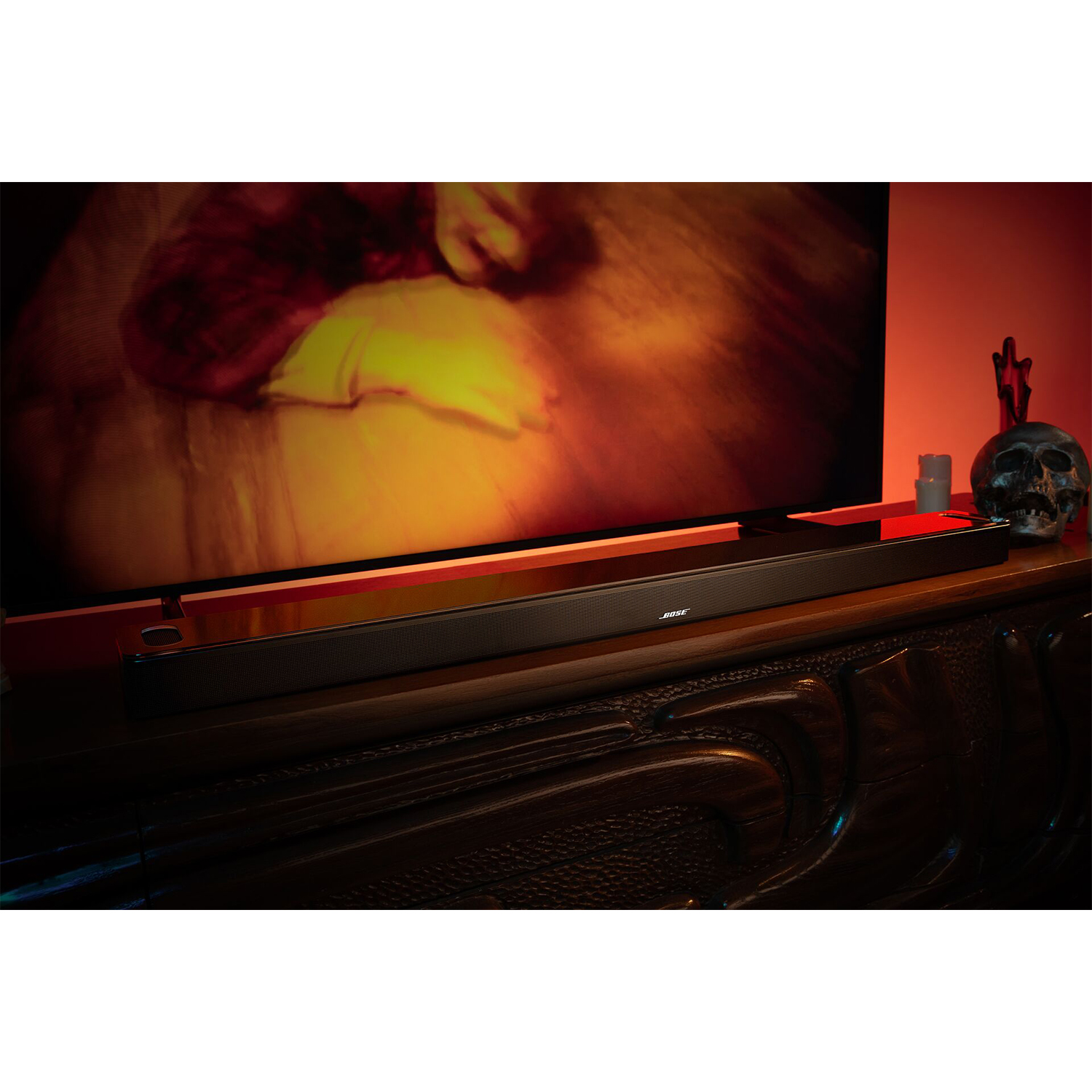Schwarzer Bose Soundbar auf einem Holzregal mit einer TV-Leinwand, Totenkopf und Kerzen.