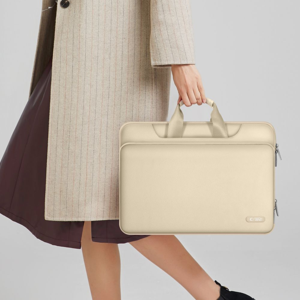 Eine Frau in einem beigen Mantel trägt eine cremefarbene Laptoptasche.