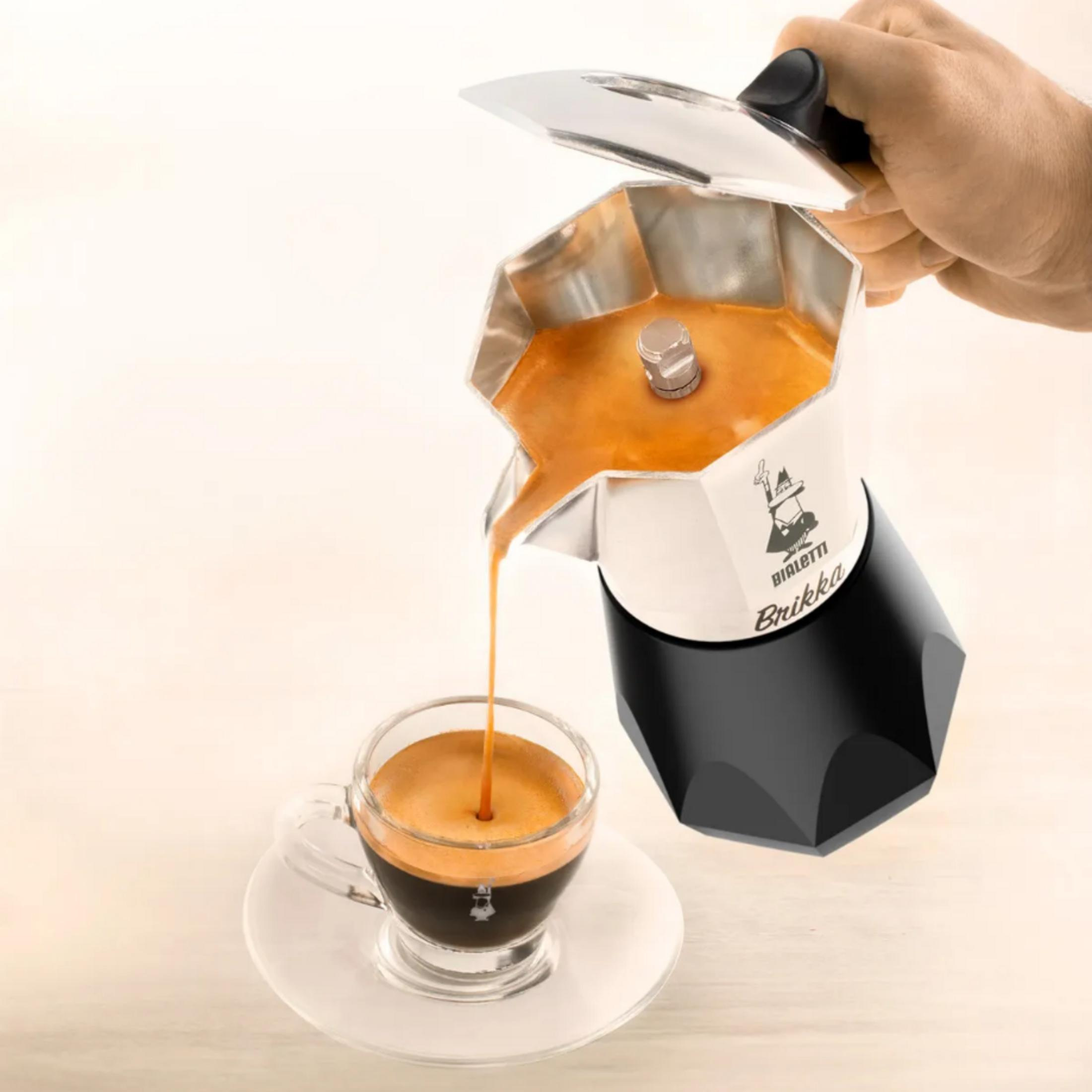 Dłoń nalewa kawę z kawiarki Bialetti do szklanki.