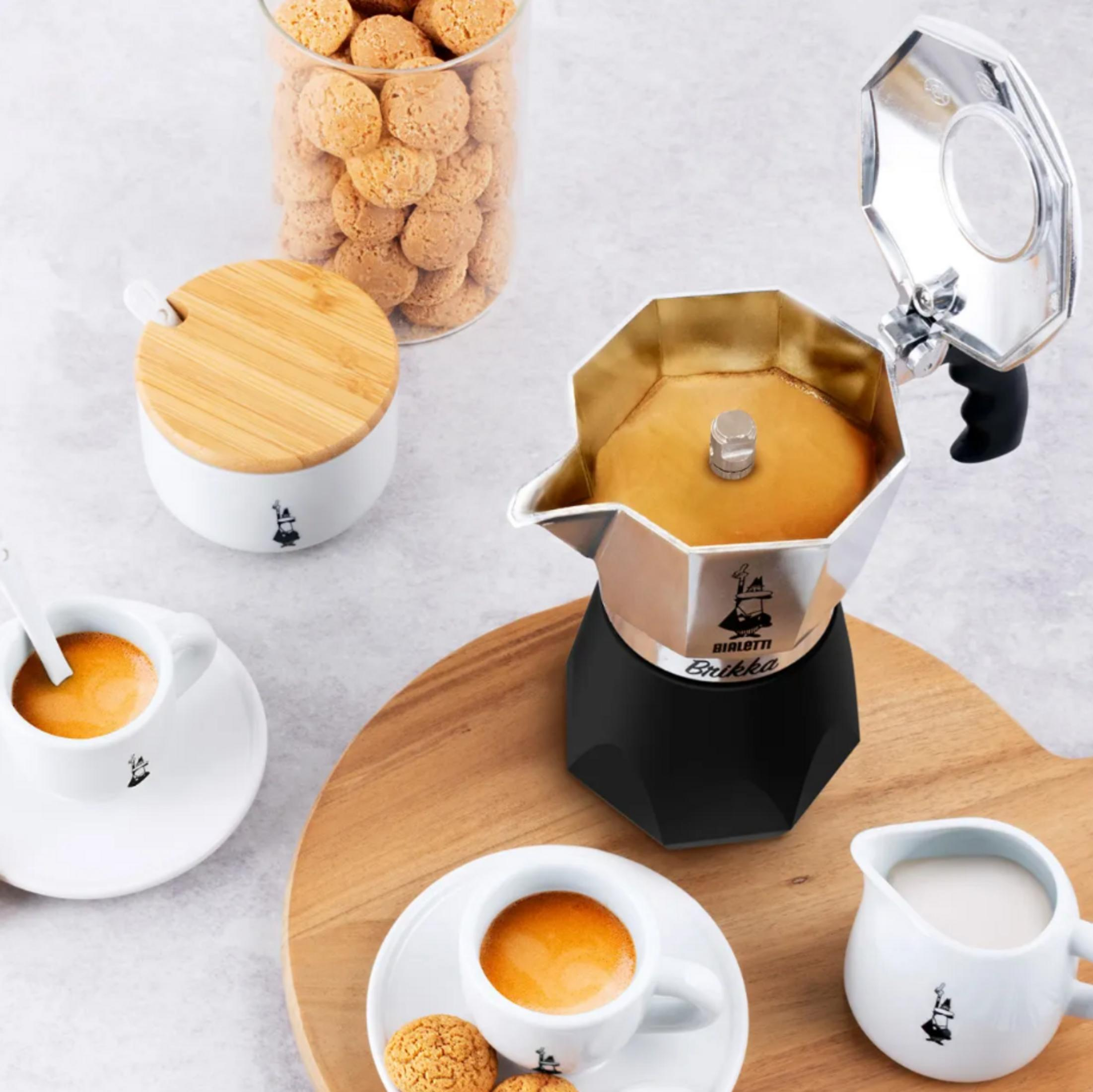 Kawiarka z filiżankami do espresso, ciasteczkami, dzbankiem na mleko i słoikiem.