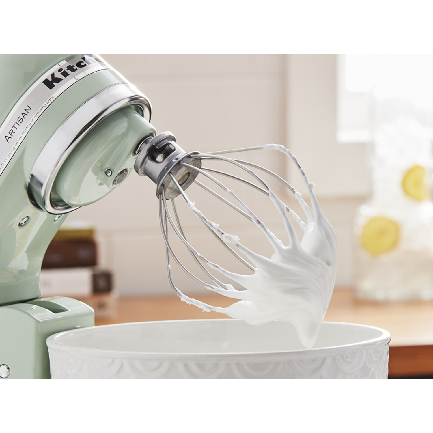 Grüner Küchenmixer mit Schneebesen und Eischnee über weißer Schüssel.