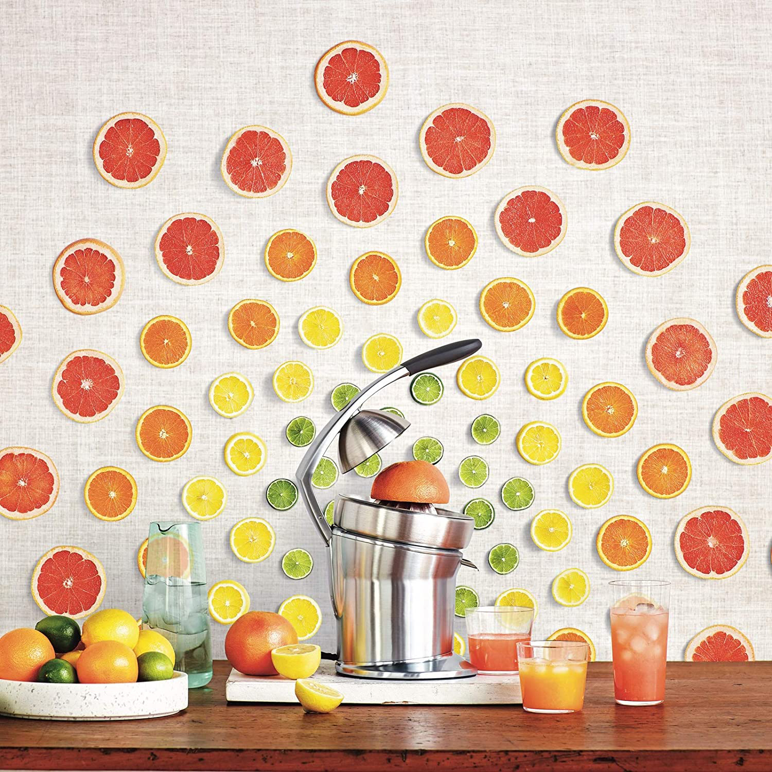 Owoce cytrusowe, wyciskarka i napoje na drewnianym stole przed ścianą z plasterków owoców.