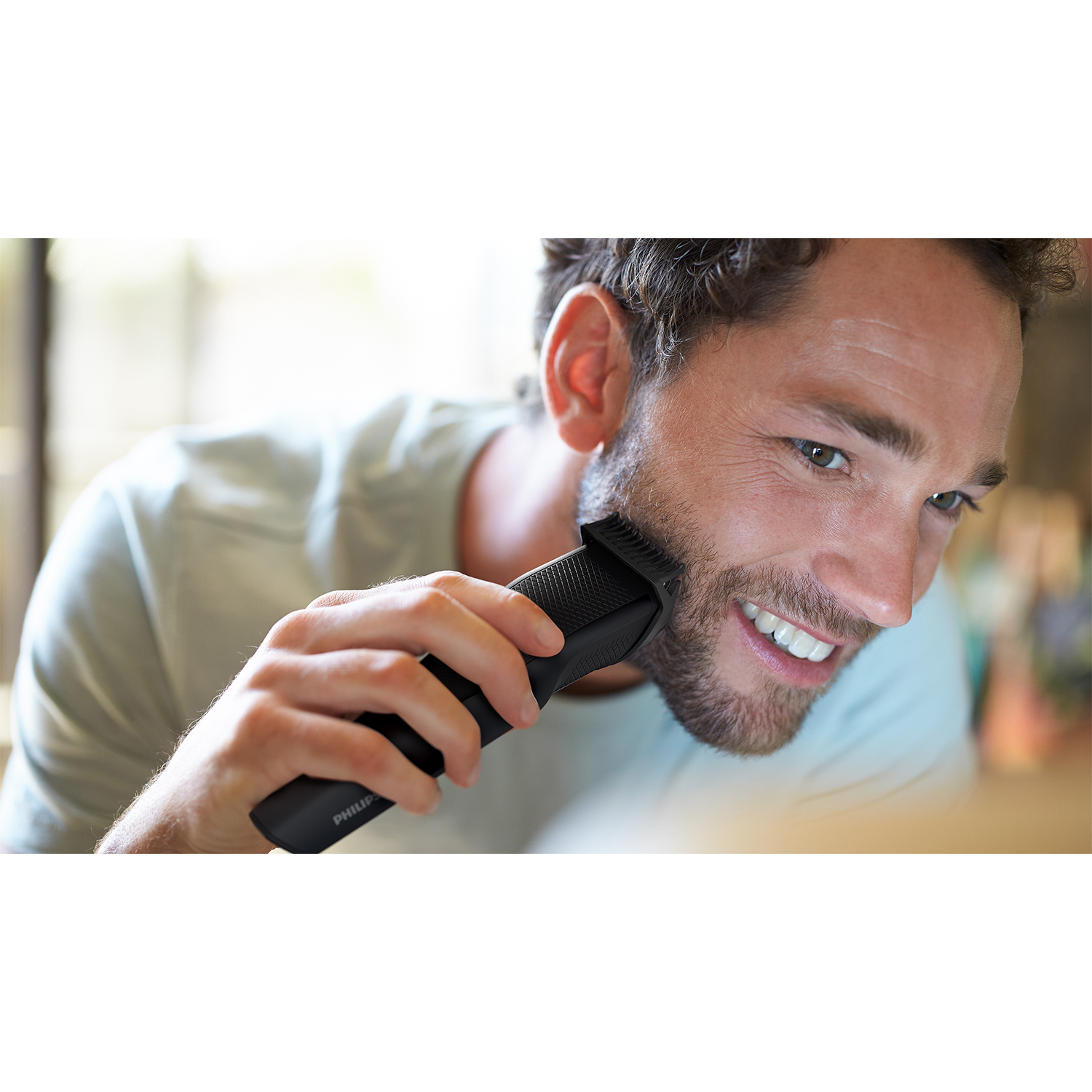 Mężczyzna przycina brodę czarną maszynką Philips. Zbliżenie.