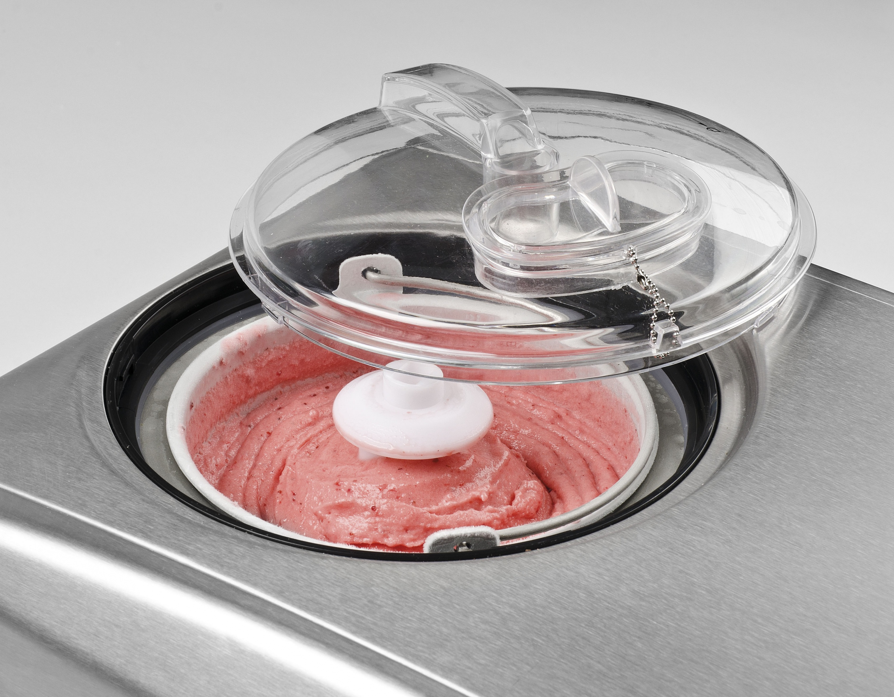 Maszyna do lodów z lodami truskawkowymi pod przezroczystą pokrywką.