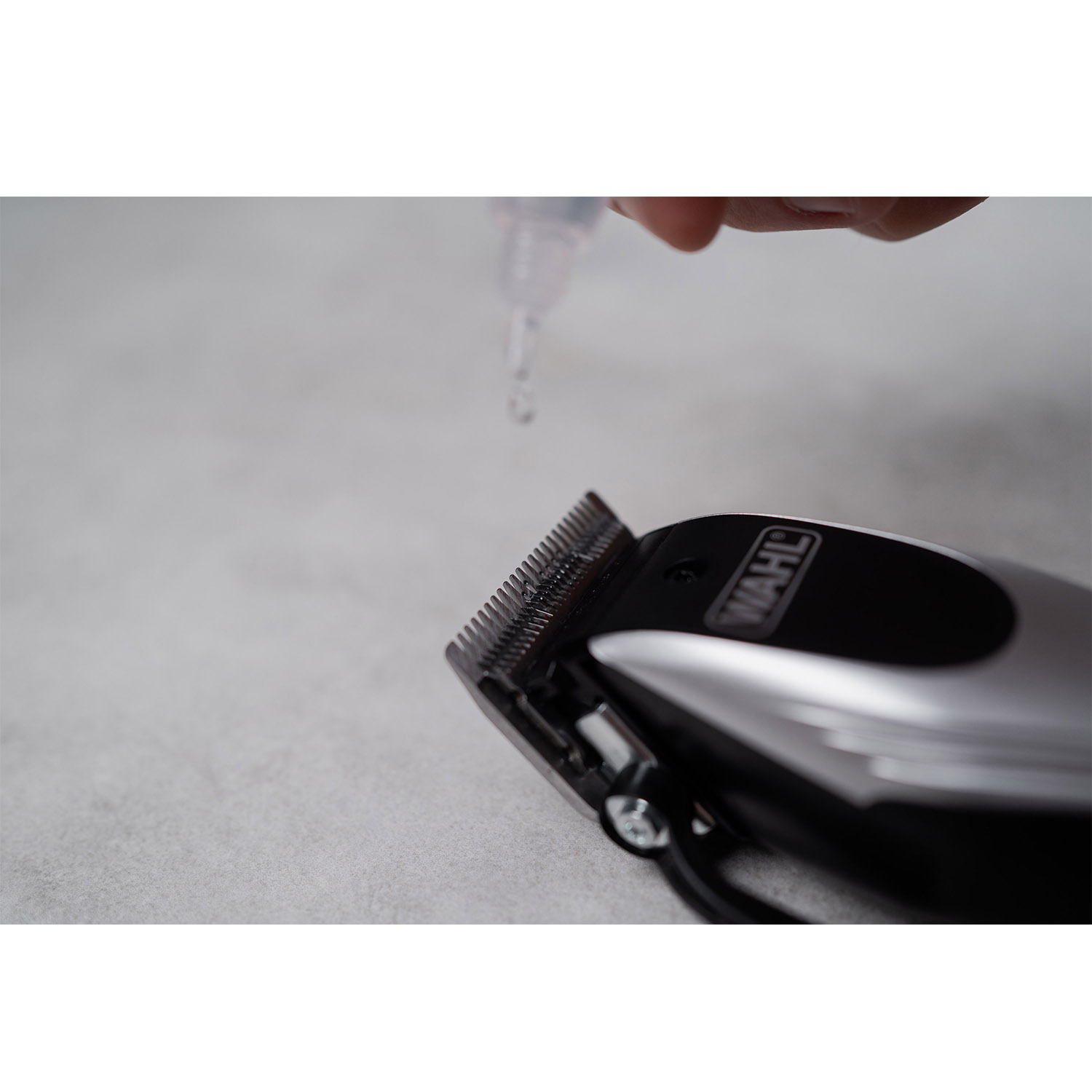 Kropla oleju spada na ostrza maszynki do strzyżenia Wahl na szarej powierzchni.