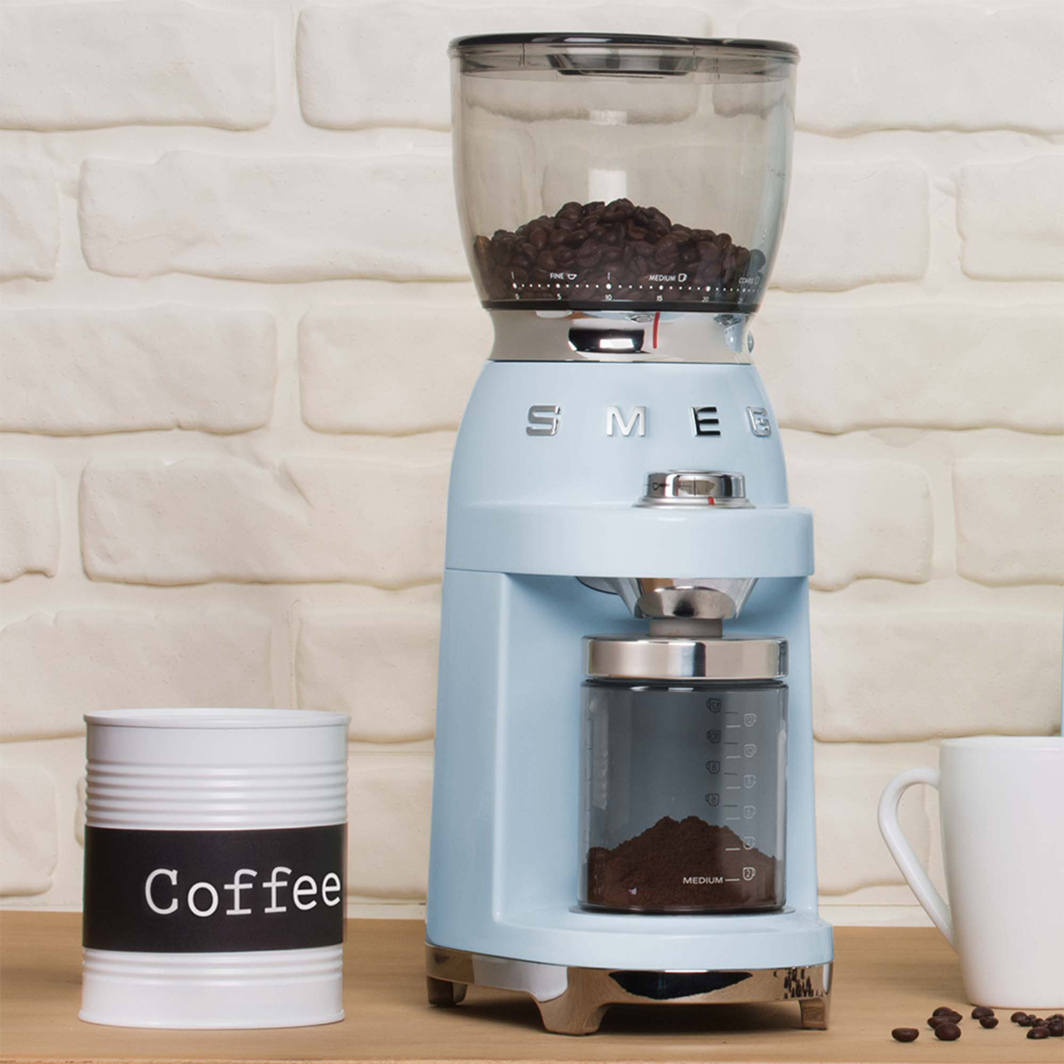 A light blue coffee grinder stands next to a coffee can on a wooden table.