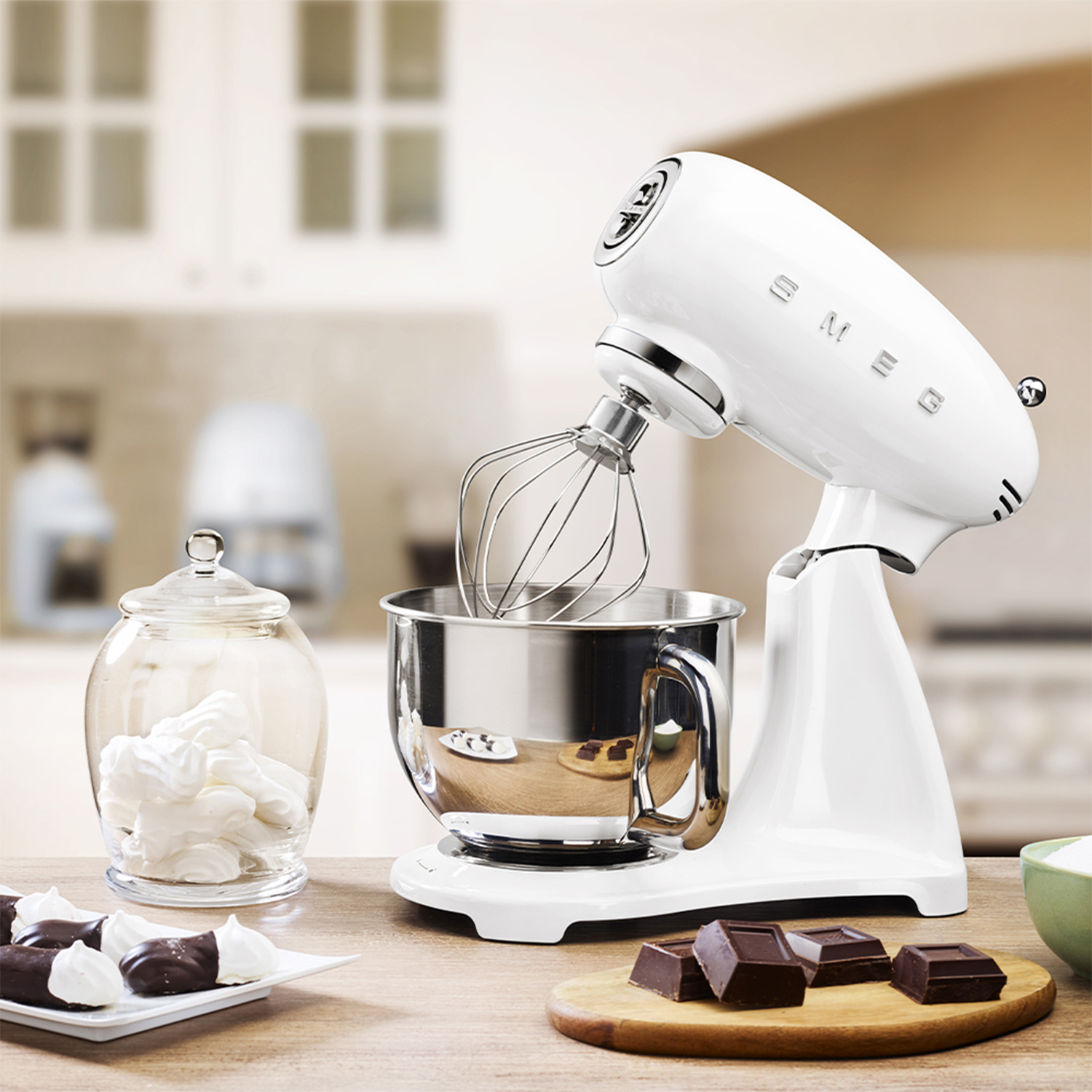 Una planetaria Smeg bianca con frusta, accanto a un barattolo di meringhe e cioccolato.